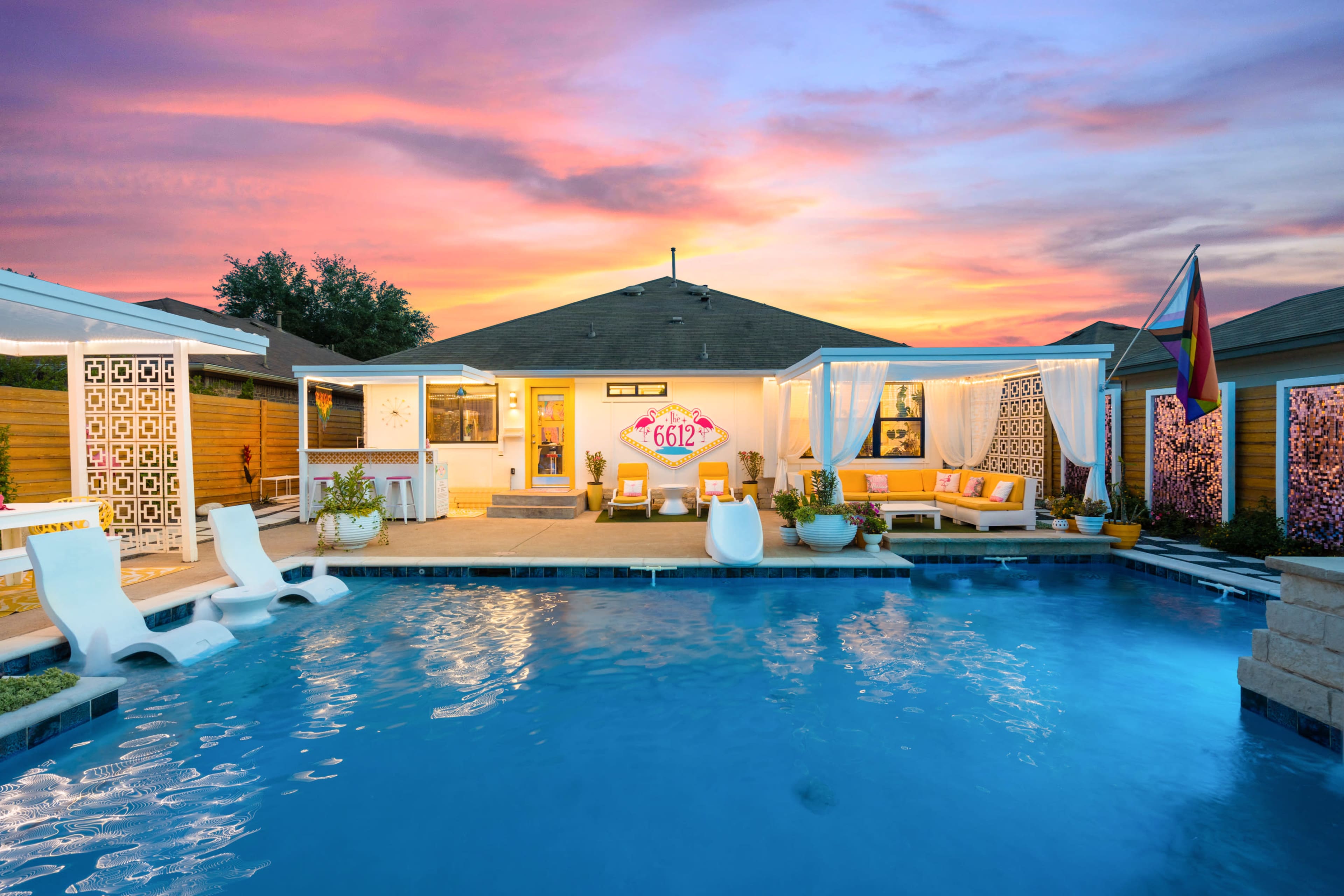 The image showcases a modern backyard with a swimming pool, colorful sunset, tropical landscaping, and lounge areas adjacent to a house.