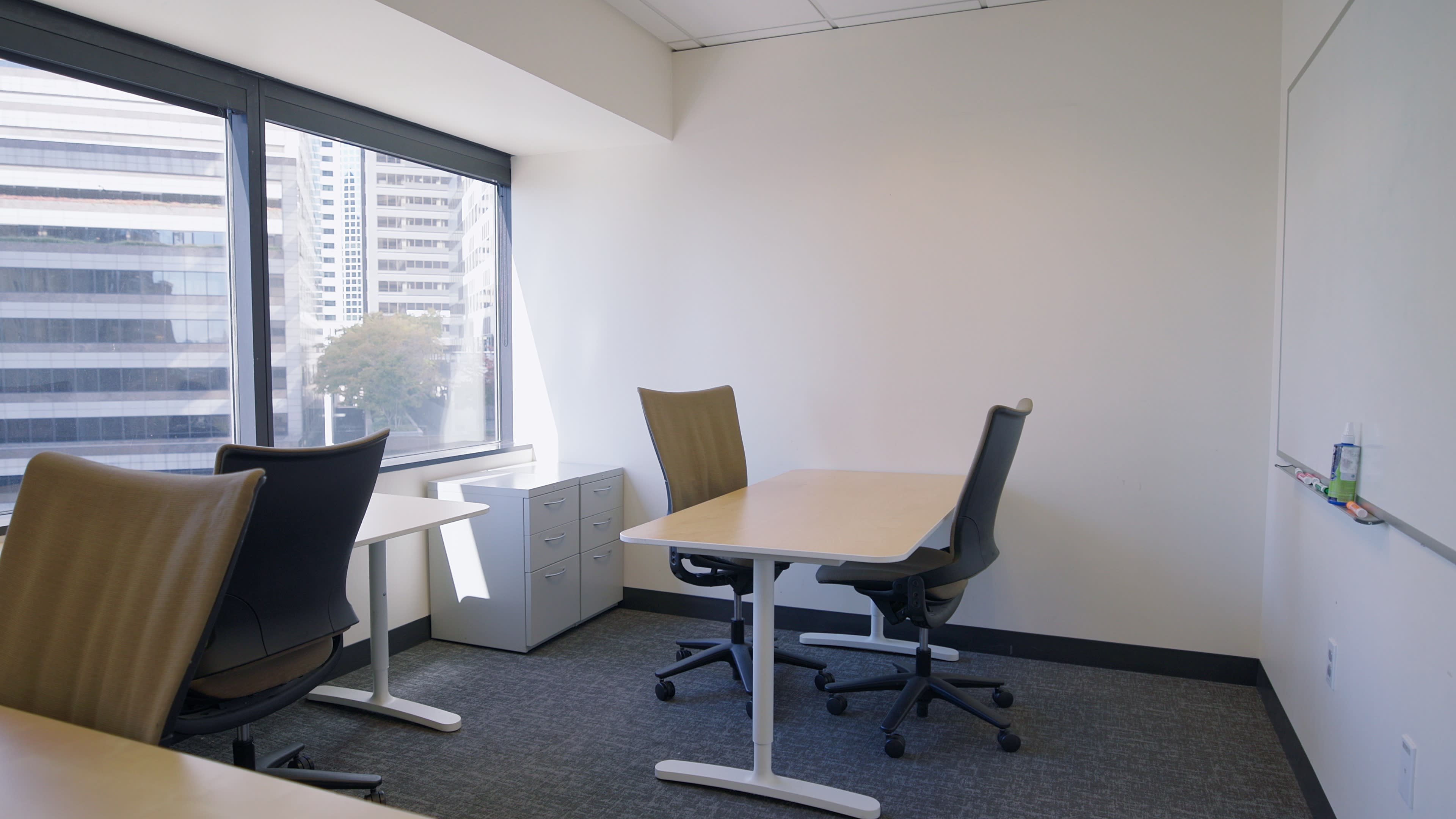 The image shows a corner office with two chairs and desks, a filing cabinet, and a large window overlooking a cityscape.