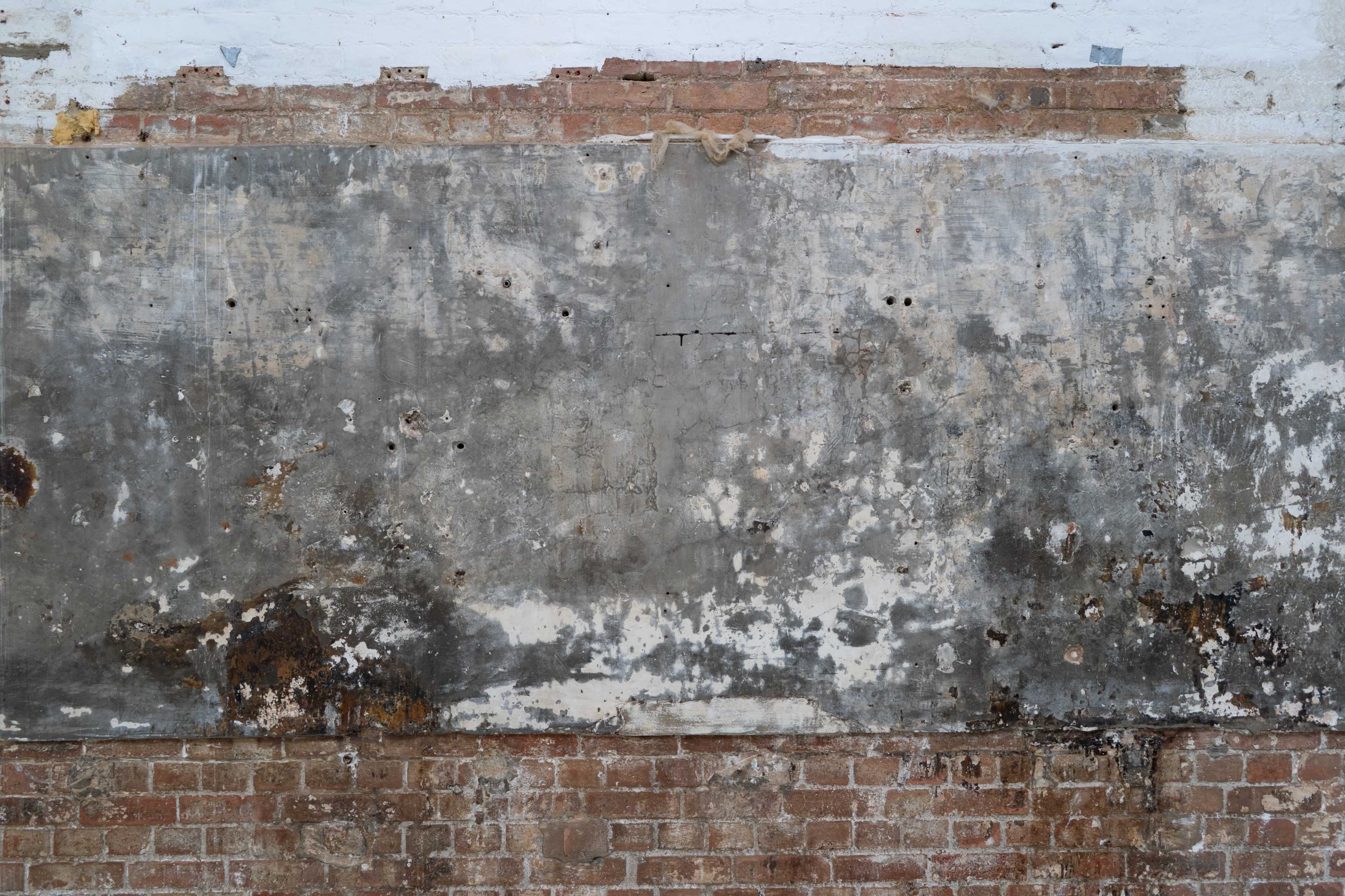 The image shows a weathered wall with peeling paint, exposed brick, and signs of wear and damage.