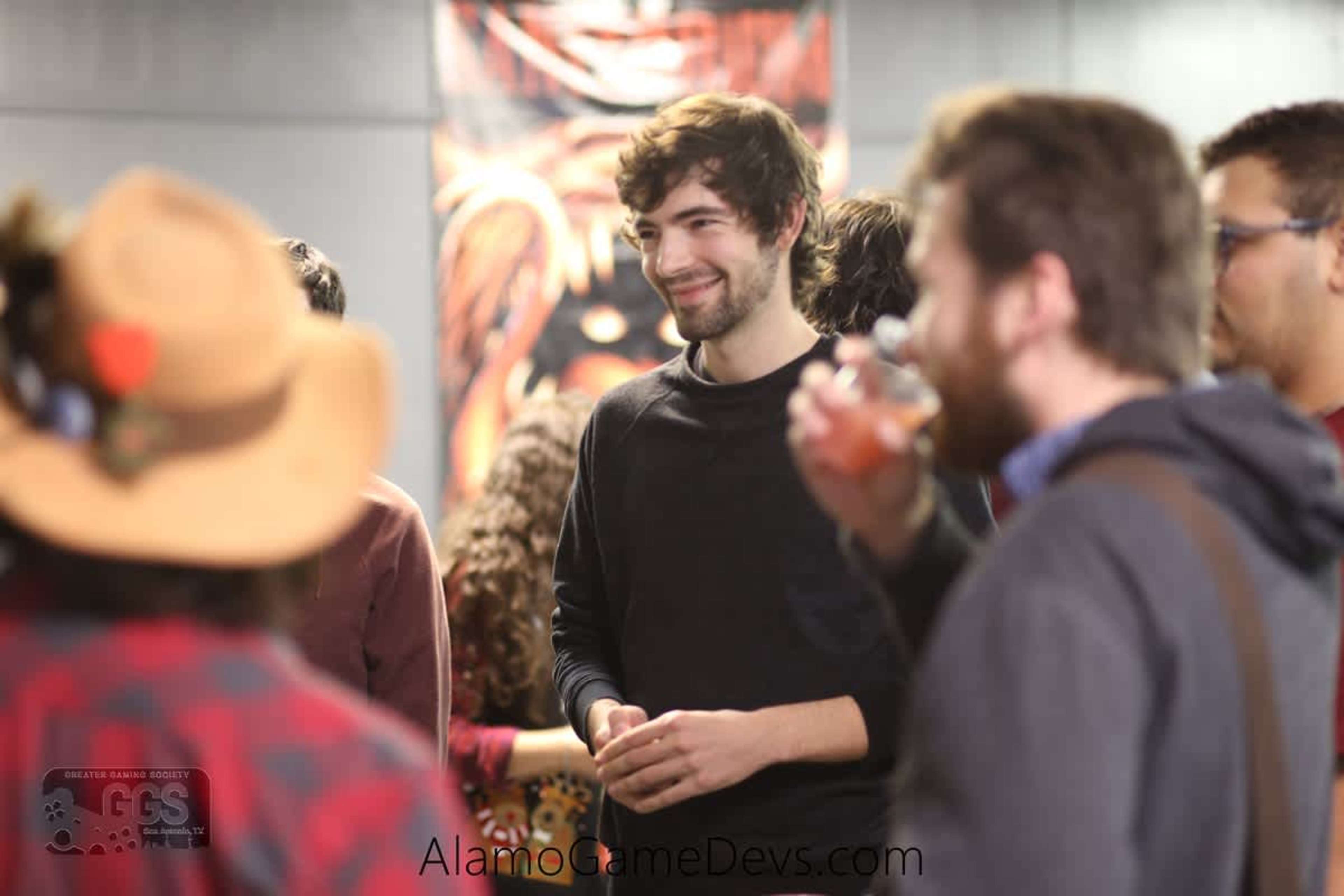 A group of people stands in a casual setting, engaging in conversation with drinks in hand.