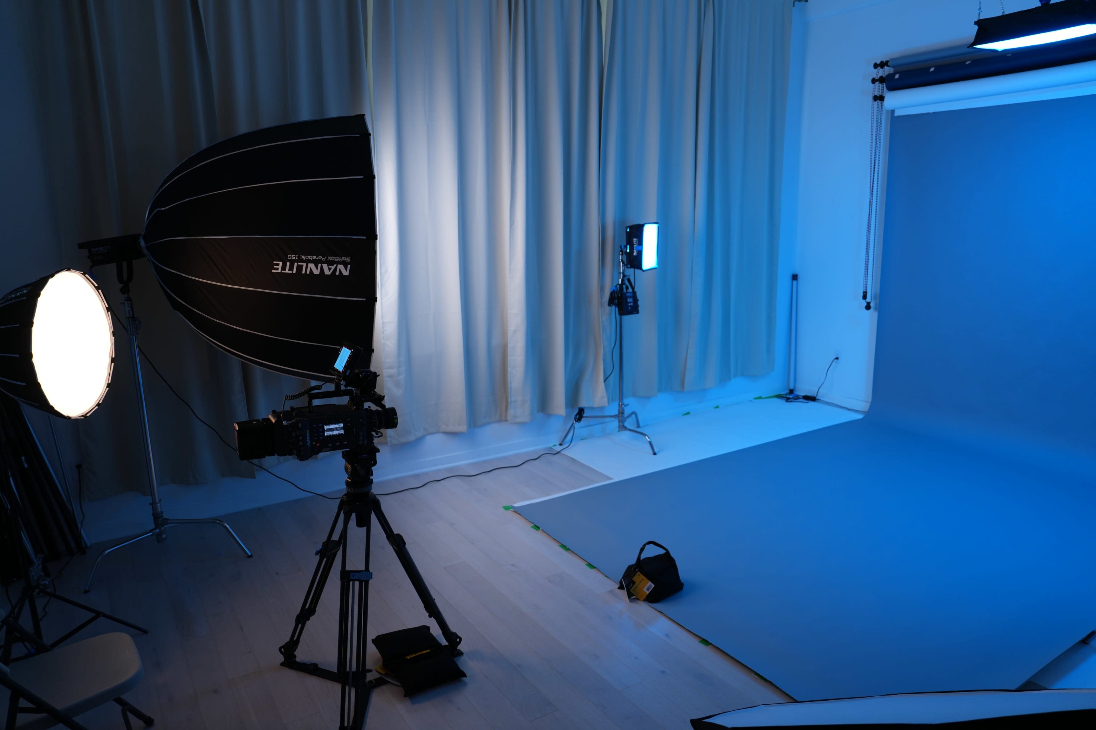 The image shows a photography studio setup with lighting equipment, a blue backdrop, and curtains.