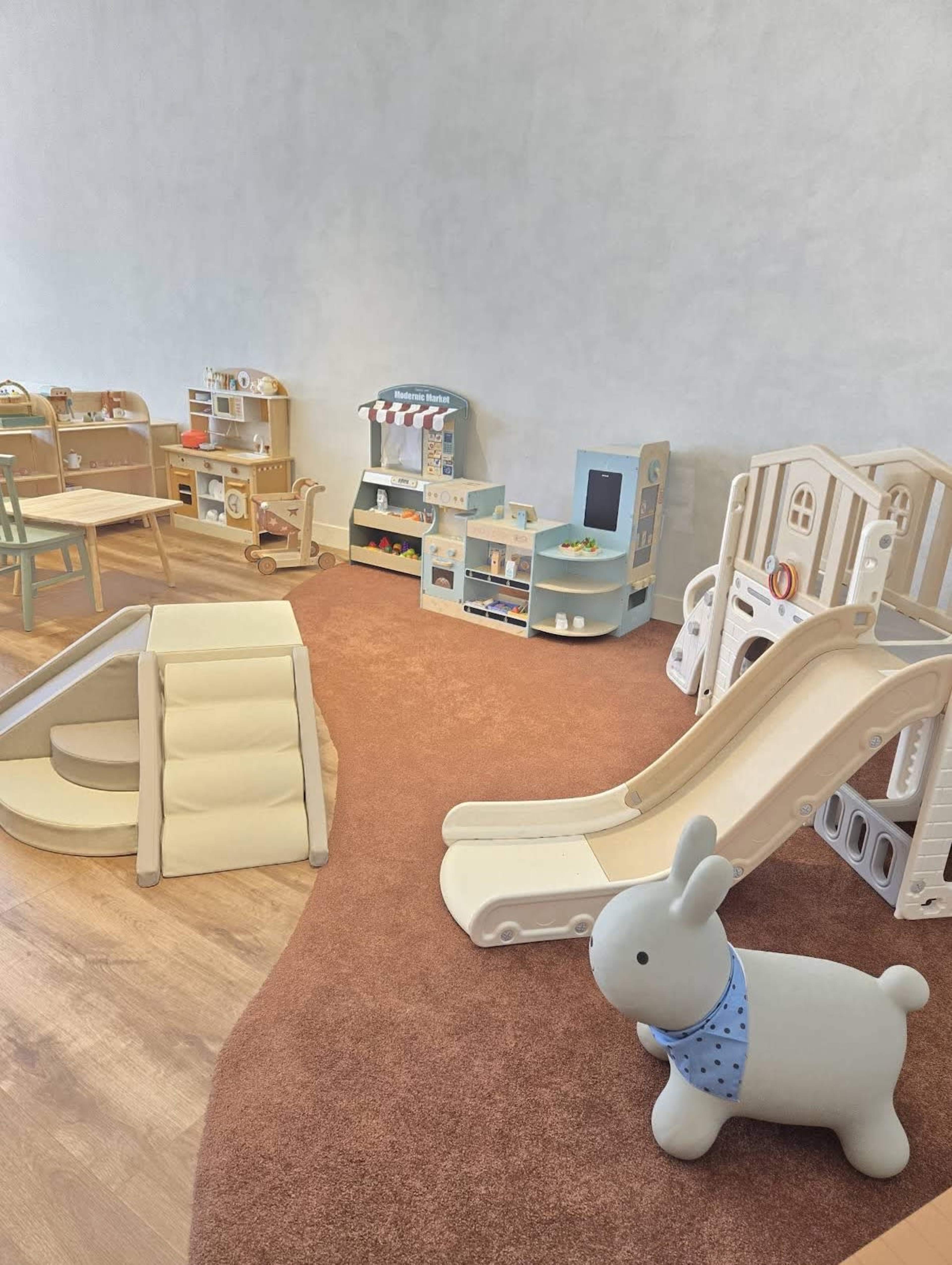 The scene features a children's play area with various play structures, including slides, climbable ramps, and wooden toys arranged on shelves.