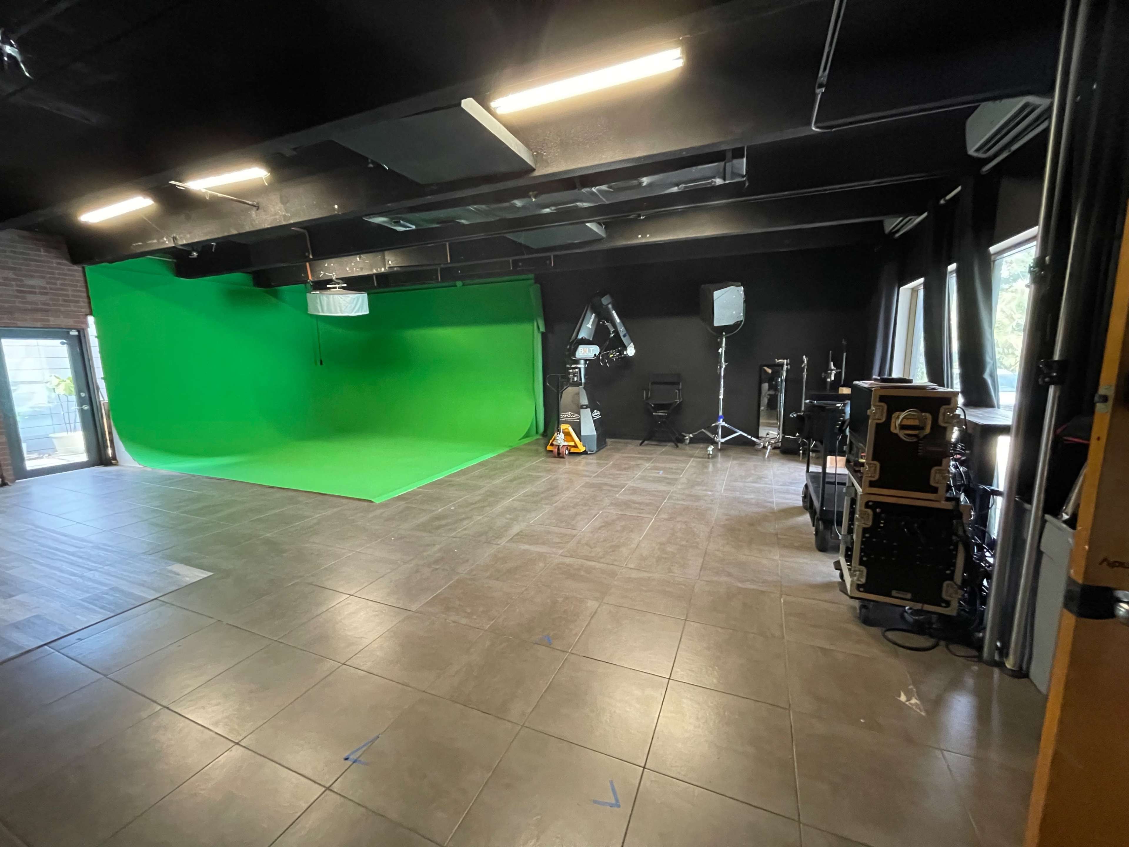A green screen studio with a bright green backdrop, lighting equipment, and various filming accessories arranged in the space.
