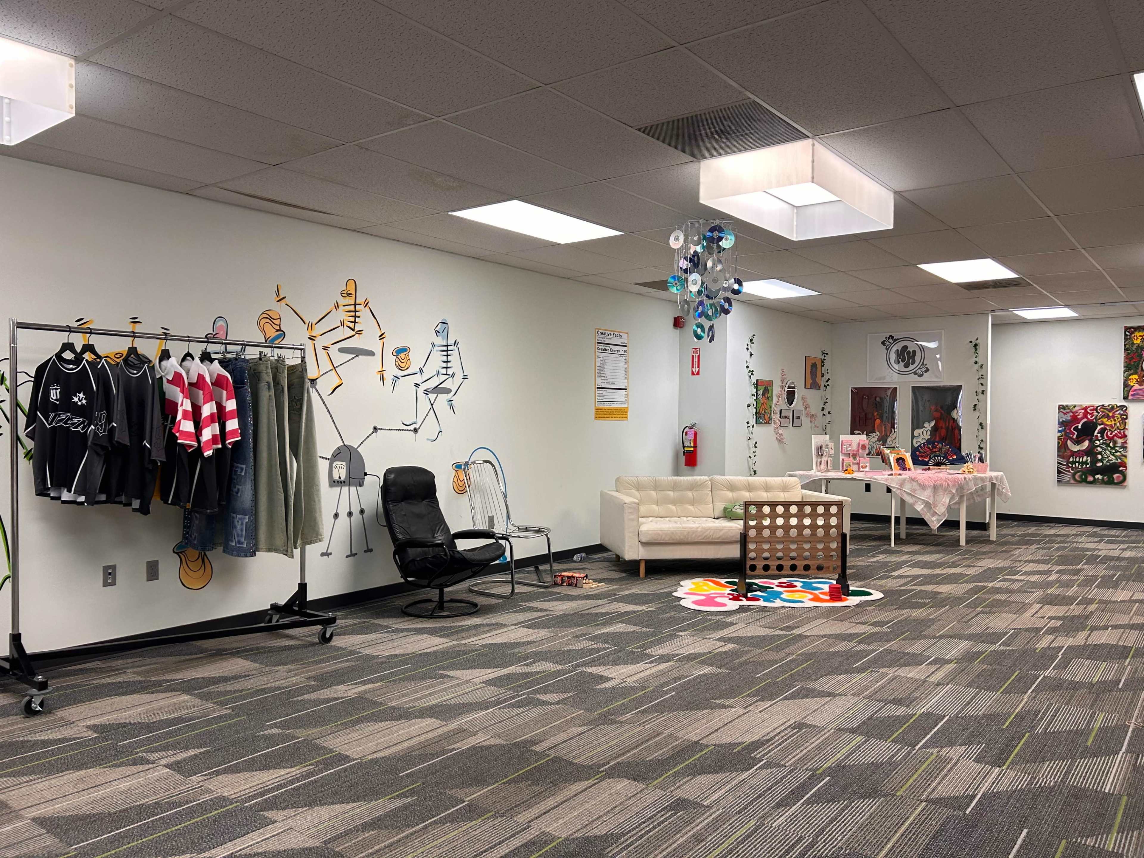The image shows a spacious room with a clothing rack, various artworks on the walls, and a seating area with a coffee table.