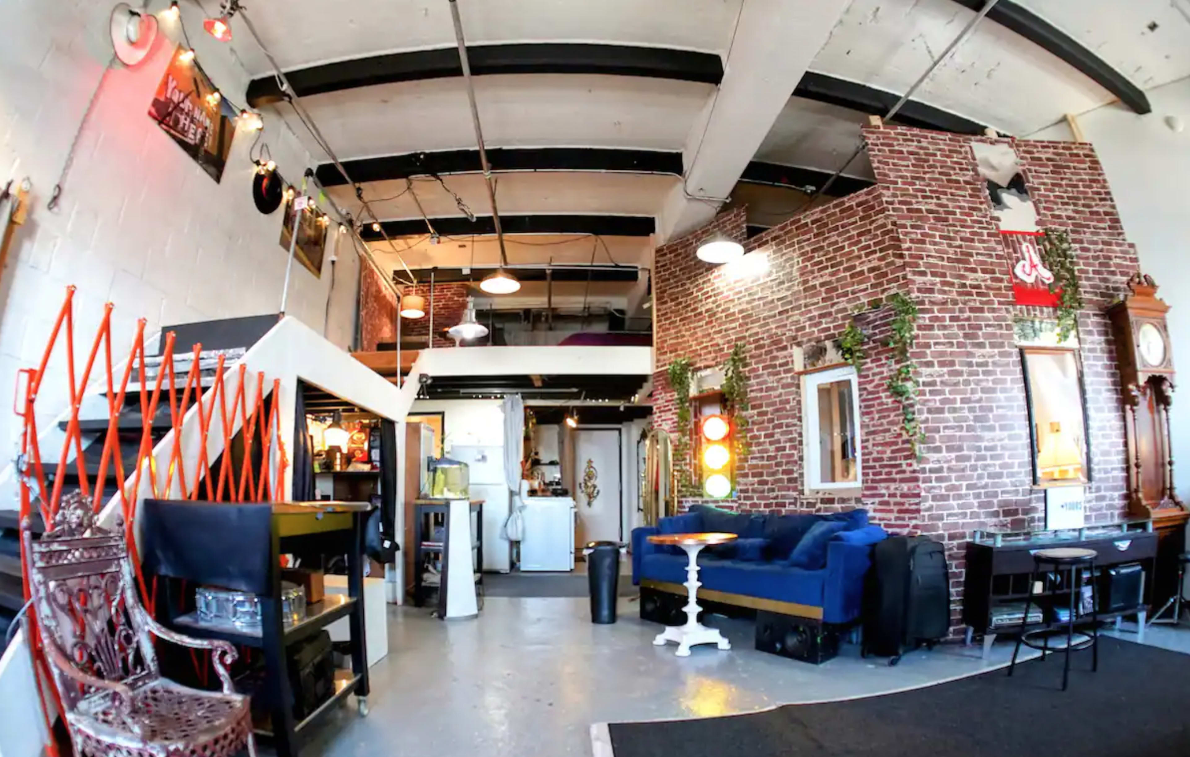 An open interior space with brick walls, a blue sofa, a kitchenette, and various seating arrangements.