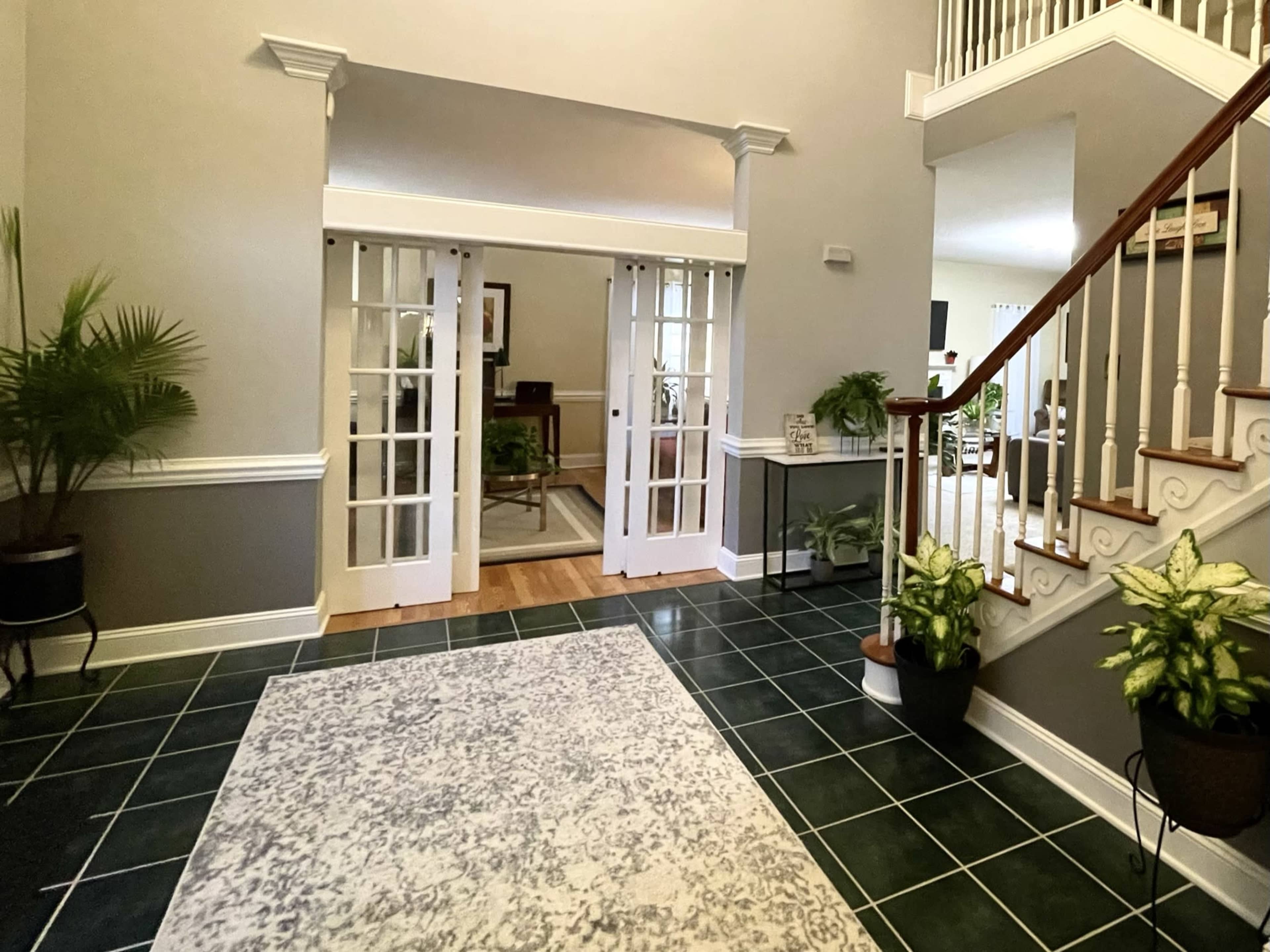 A spacious entryway featuring sliding glass doors, a staircase with wooden handrails, and potted plants on a green tiled floor.