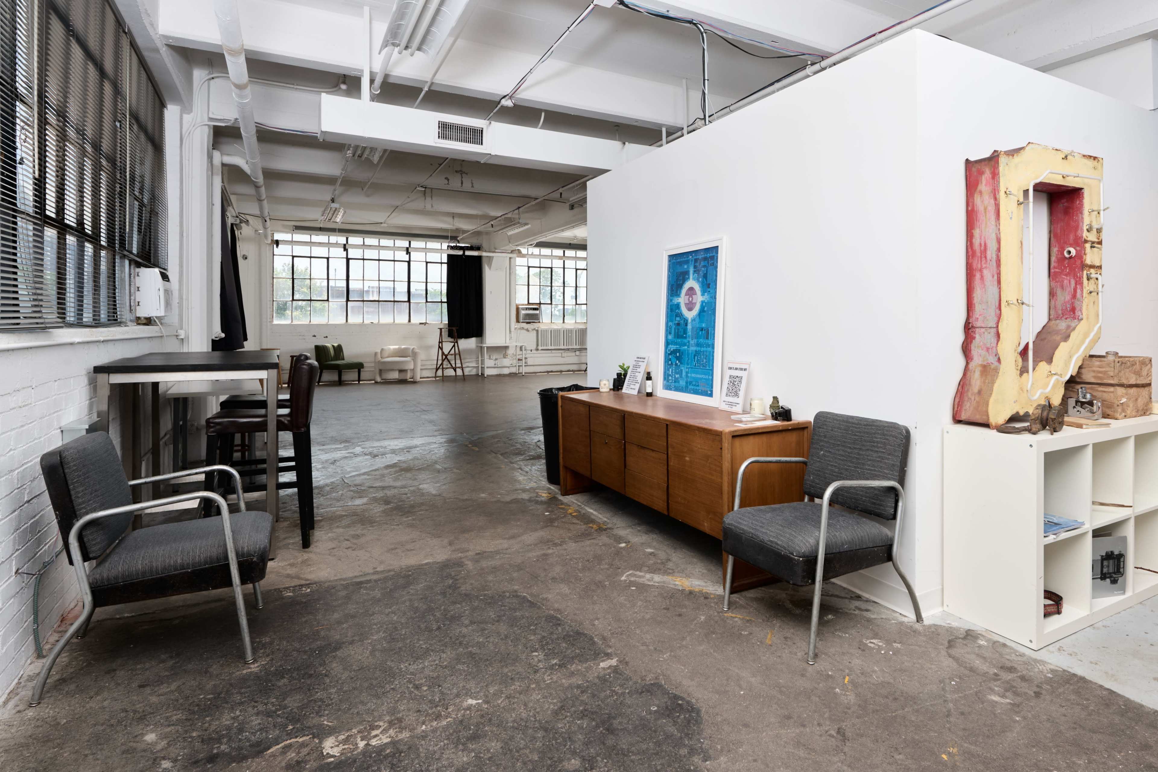 The image shows a spacious, industrial-style interior with a white partition, a wooden cabinet, and several chairs arranged in a well-lit area.