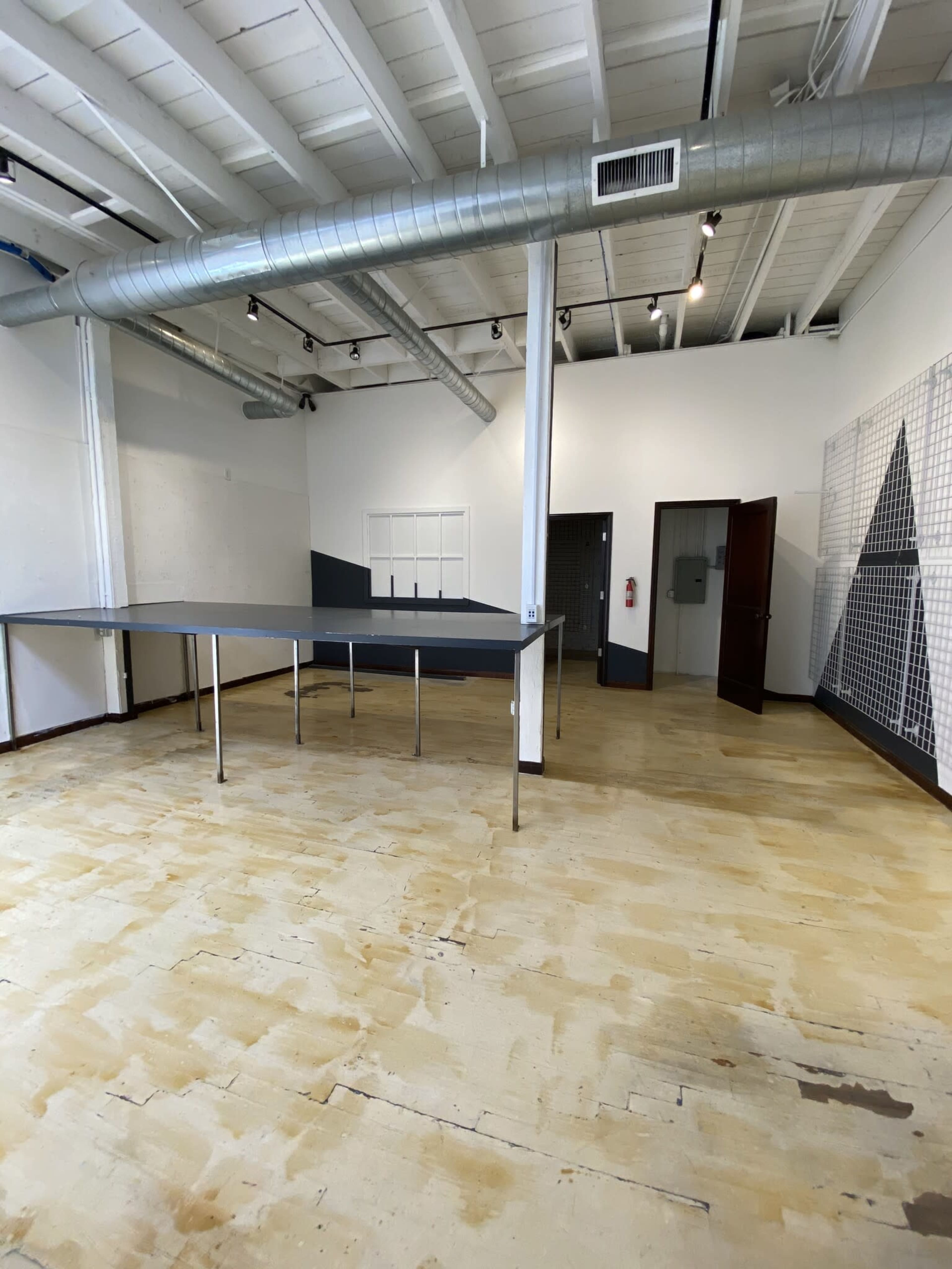 An empty room with a large table in the center, exposed beams on the ceiling, and a doorway leading to another space.