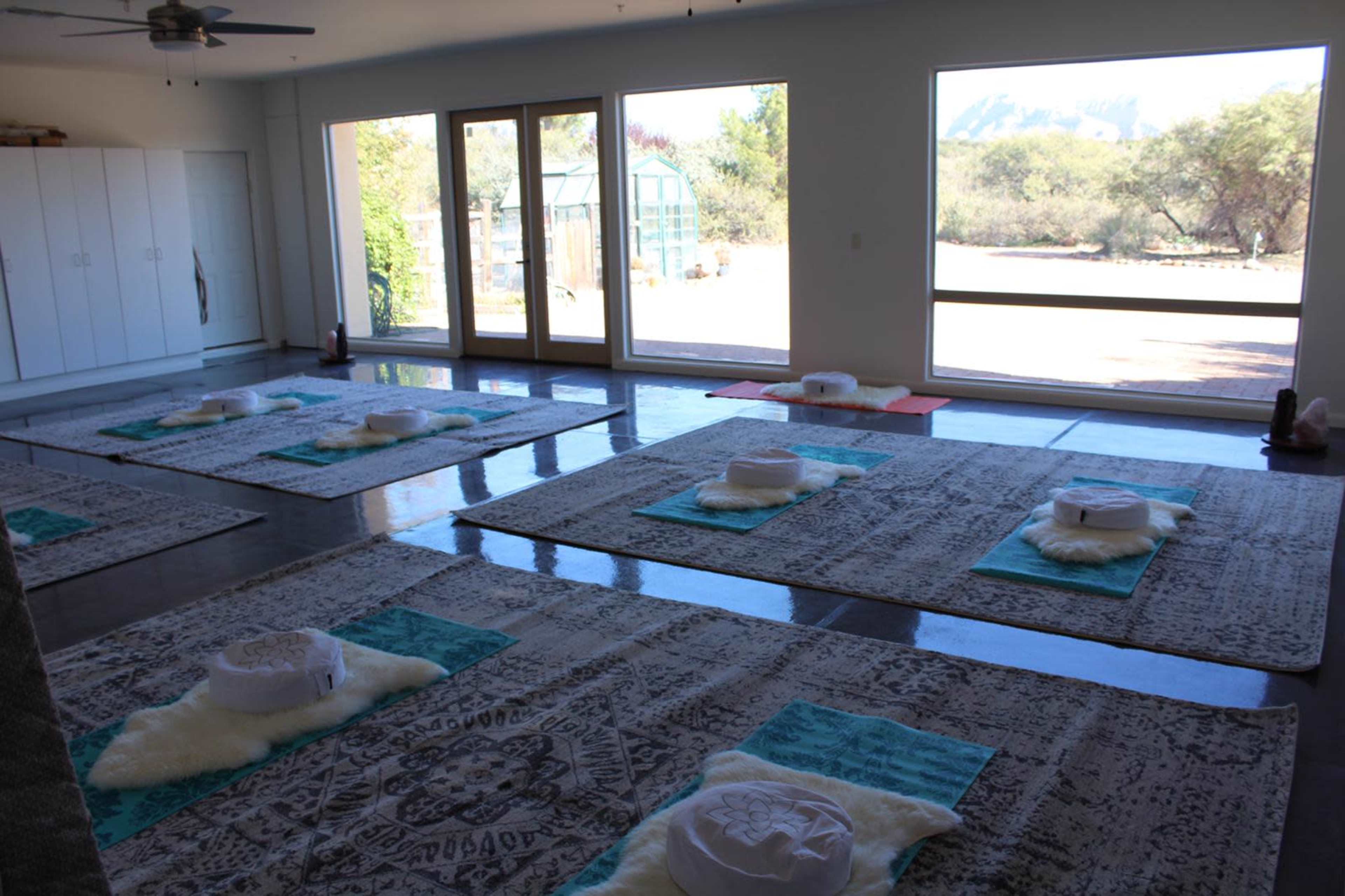 The image features a spacious yoga studio with several mats arranged on a polished concrete floor, large windows allowing natural light, and a view of the outdoors.