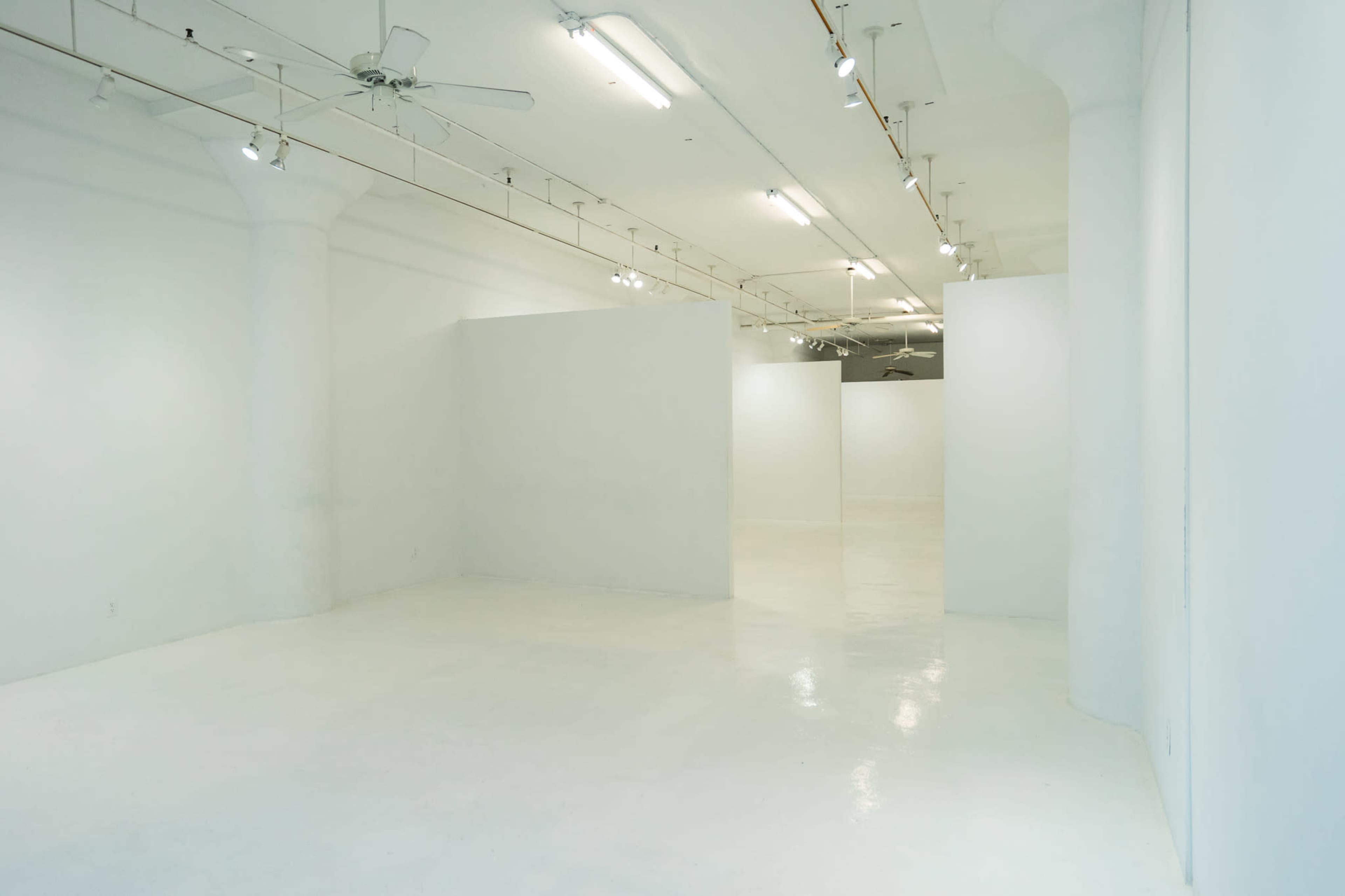 A spacious, empty room with white walls and a polished floor, illuminated by overhead lights.