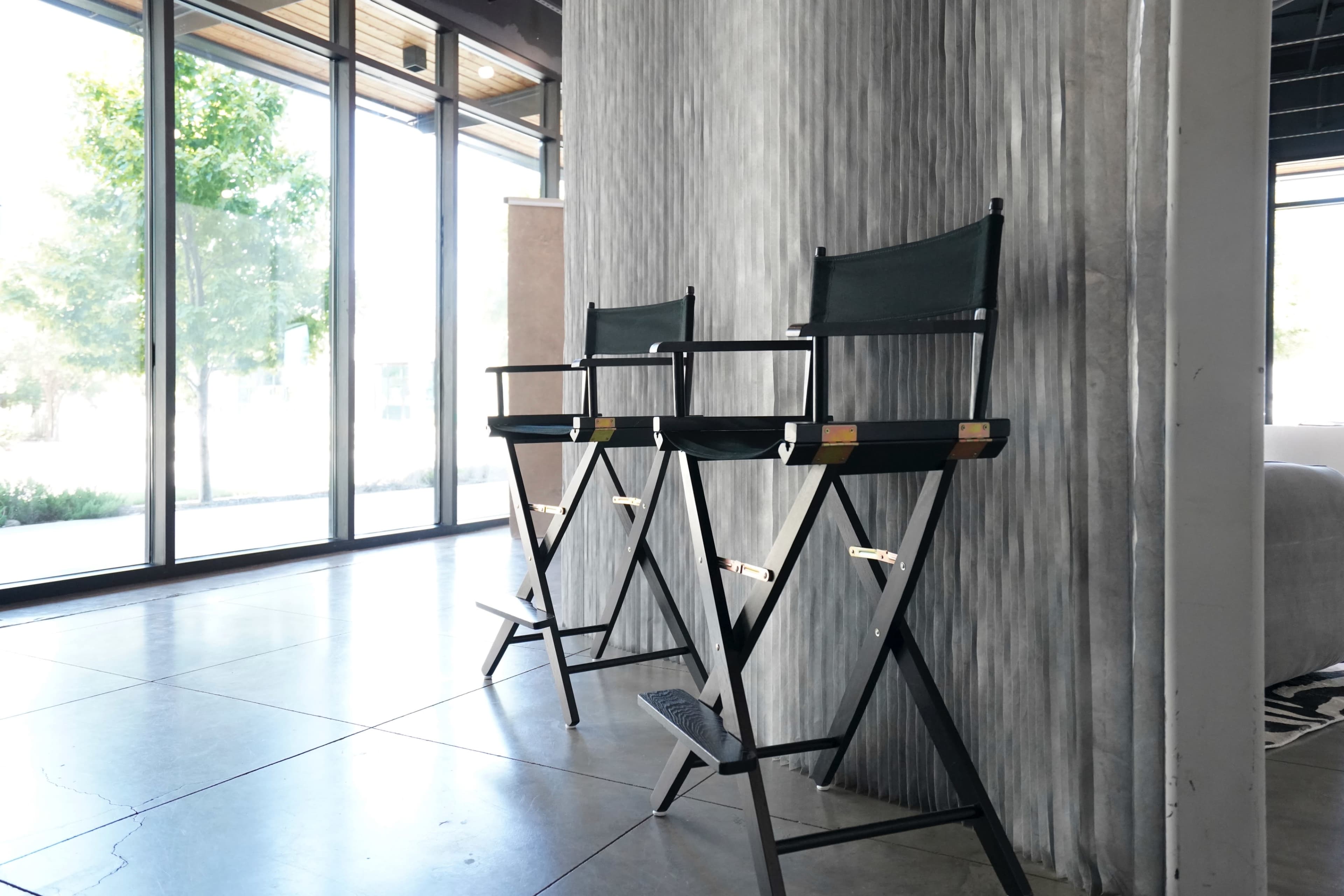 Two director's chairs are positioned next to a textured wall in a modern interior space with large windows.