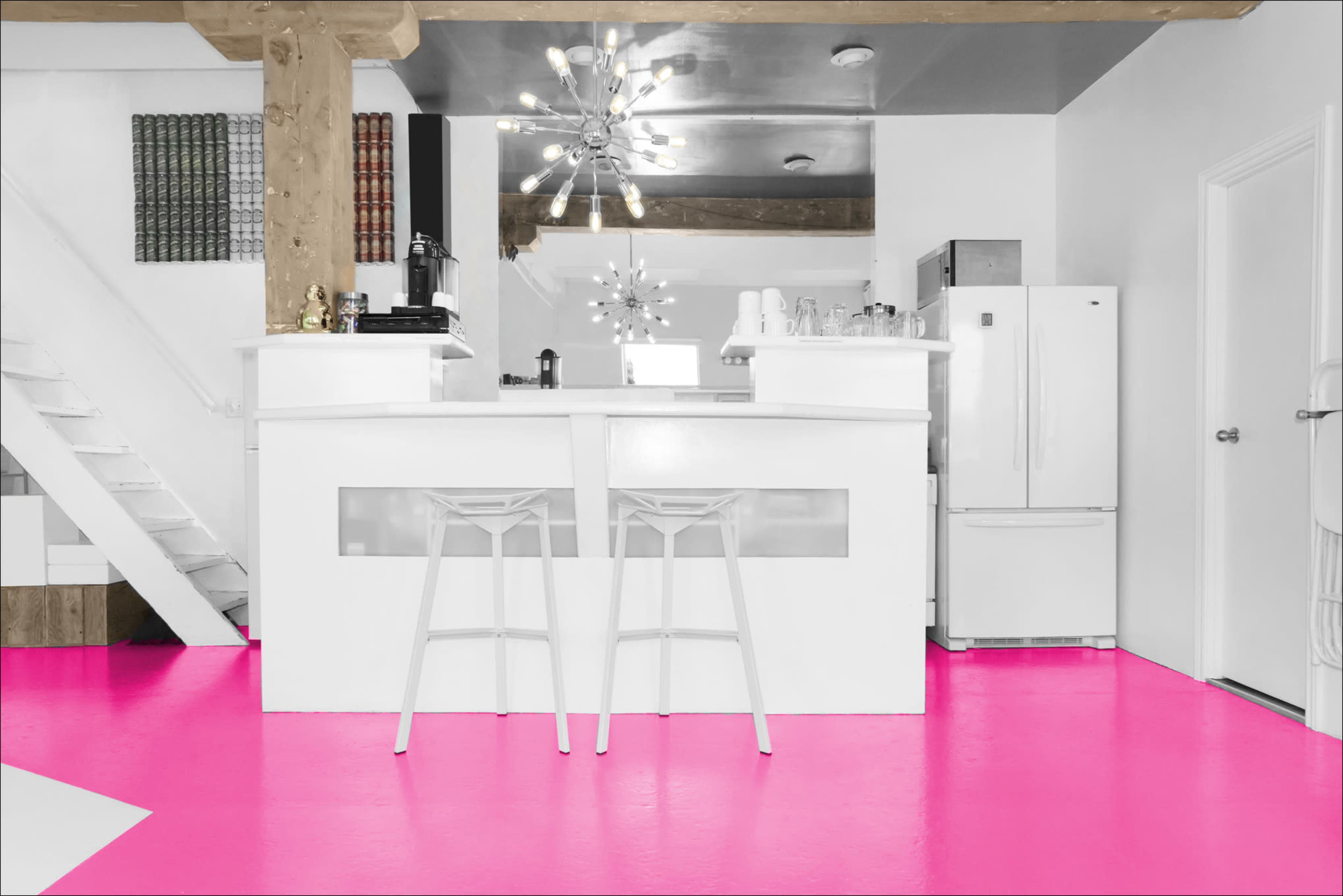 A modern kitchen with a white bar counter and stools, pink flooring, and a staircase in the background.