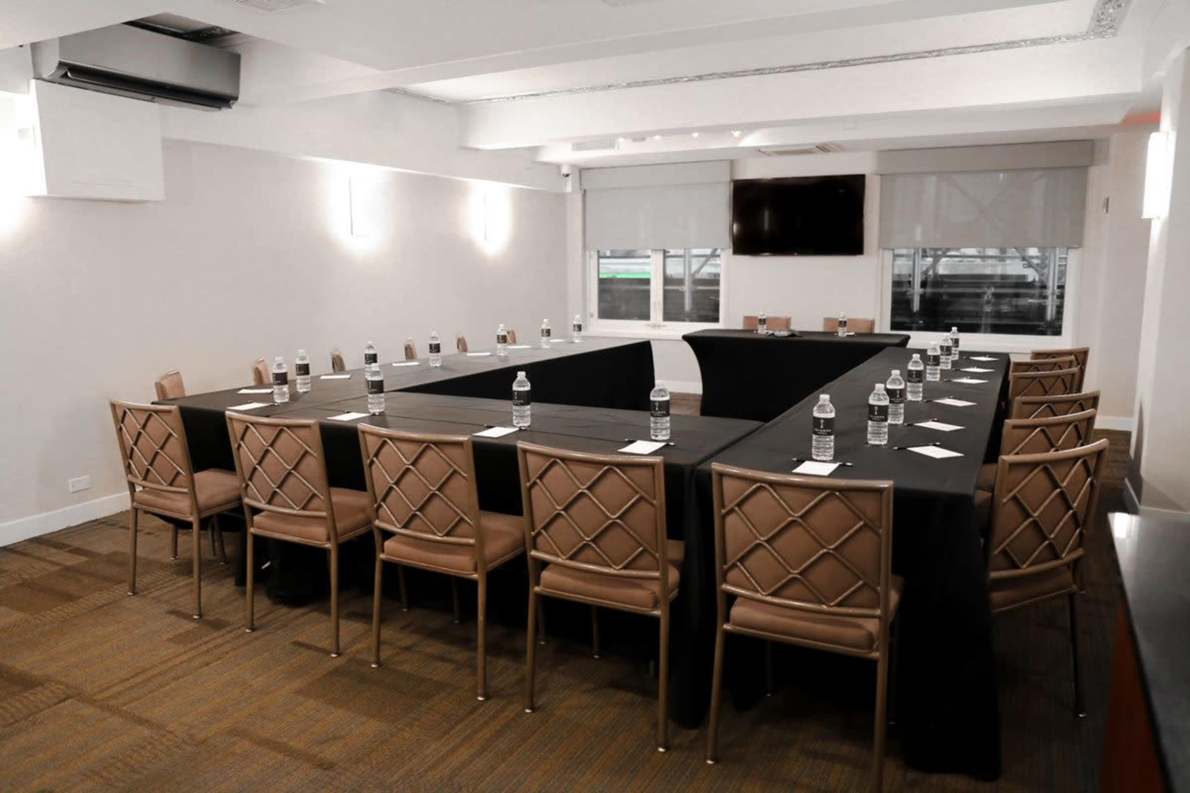 A conference room features a large rectangular table surrounded by chairs, with water bottles and notepads placed at each seat.