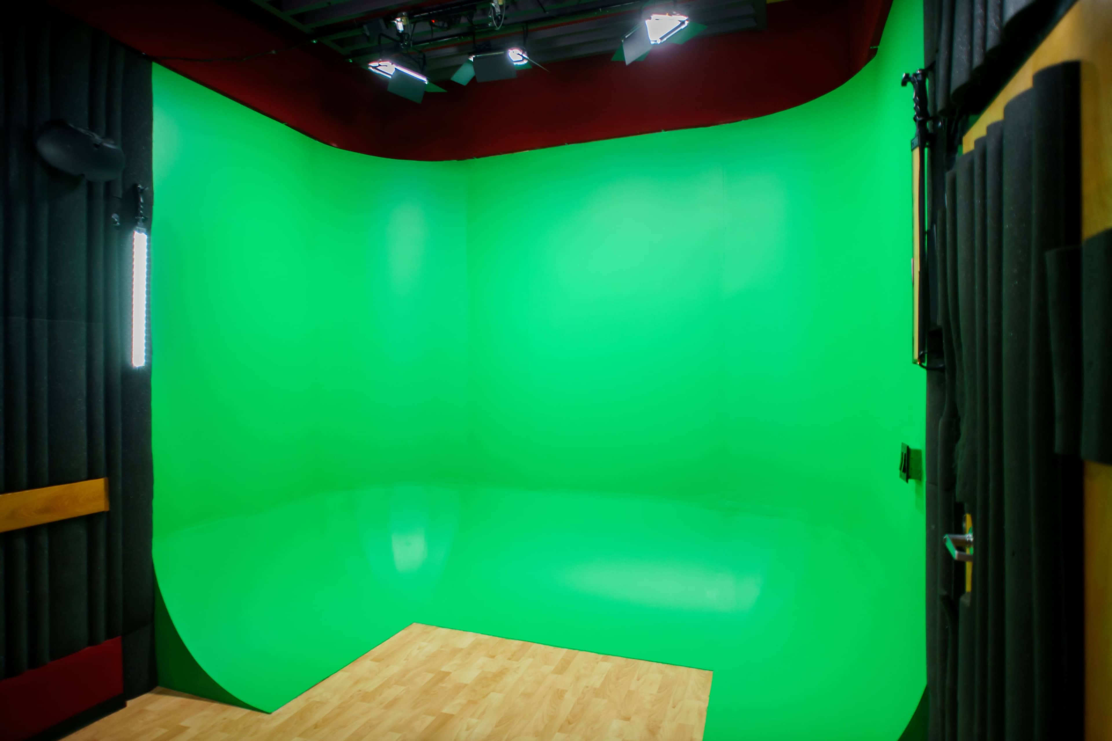 A green screen studio with a curved green backdrop and wooden flooring.