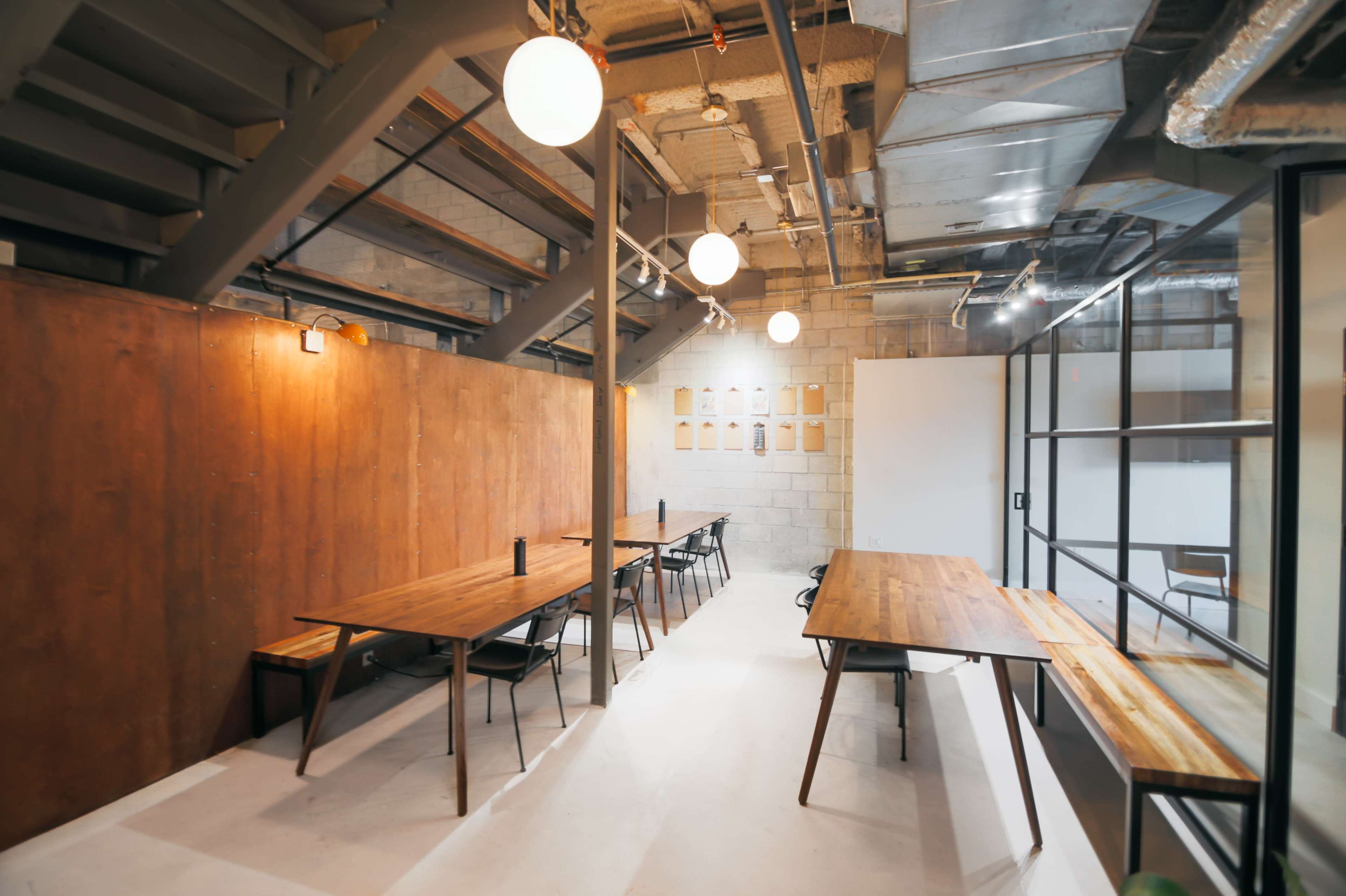 A modern workspace with wooden tables, black chairs, and overhead lighting in an industrial-style interior.