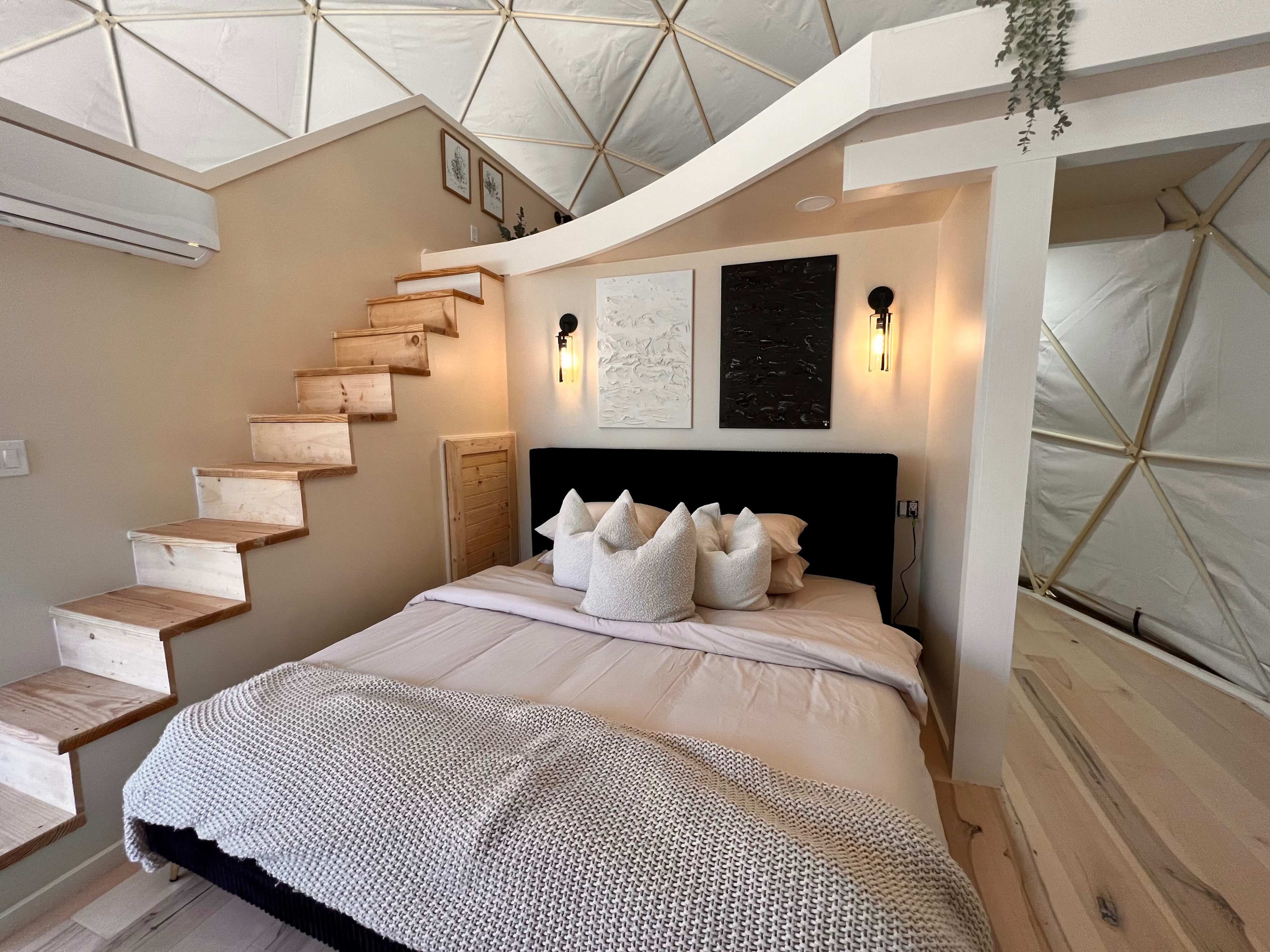 A modern bedroom with a circular ceiling, a bed with decorative pillows, and a minimalist staircase leading to an upper area.