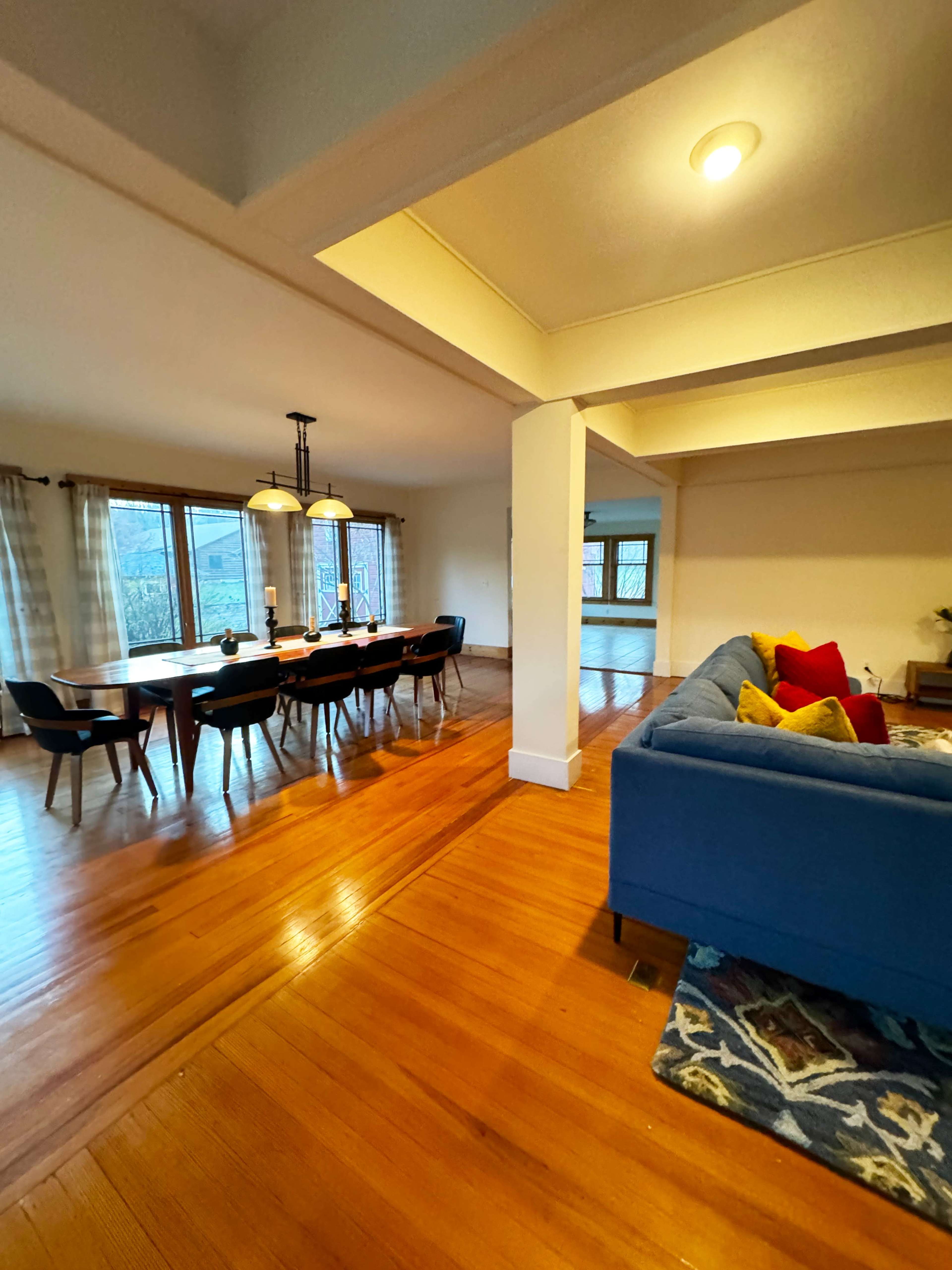 A spacious living and dining area with a blue couch, a dining table set for several people, and large windows providing natural light.