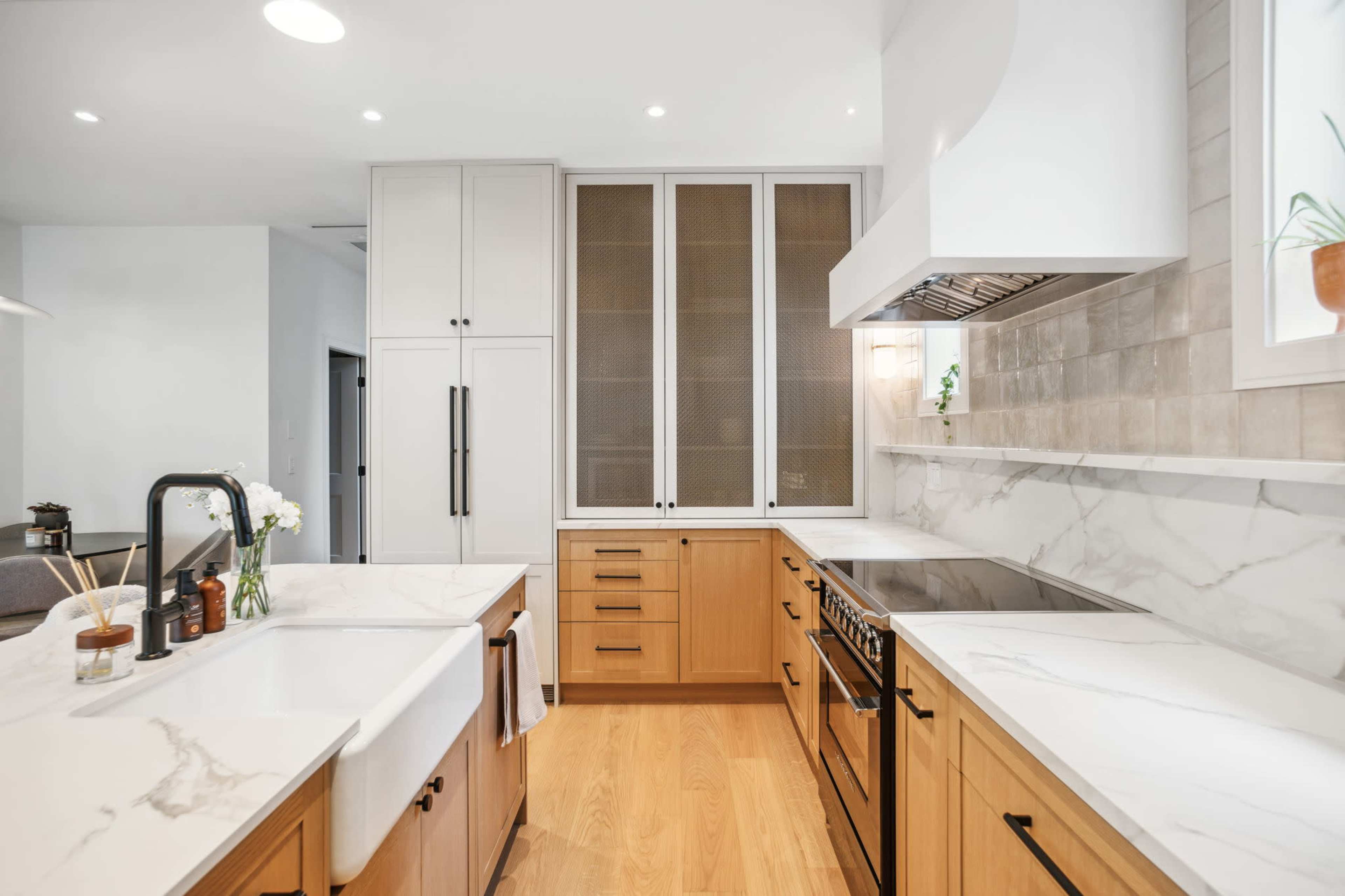 The kitchen features a combination of wooden and white cabinetry, marble countertops, and modern stainless steel appliances.