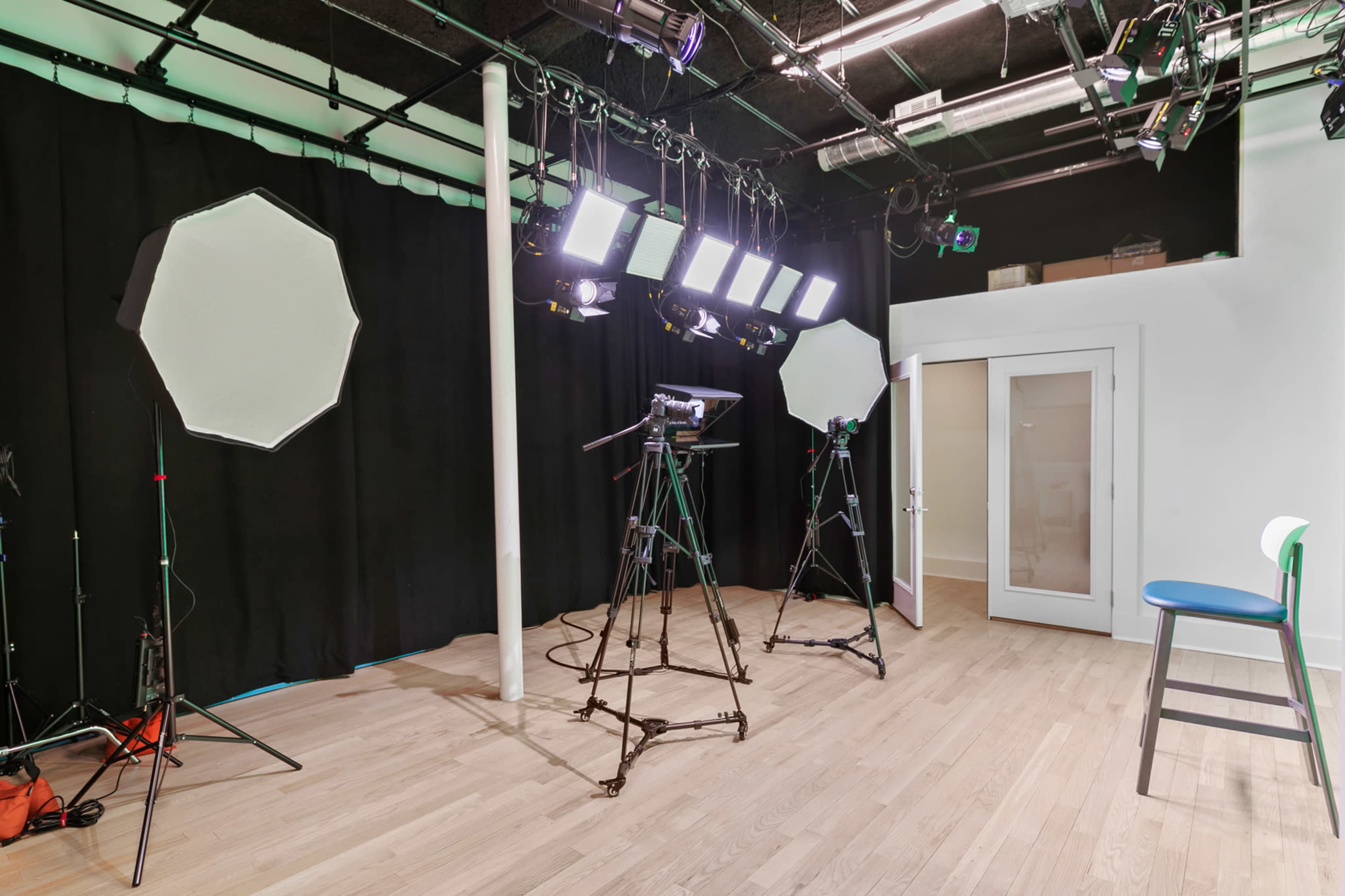 A photography studio equipped with multiple lights, three tripods, and a large empty chair against a black backdrop.