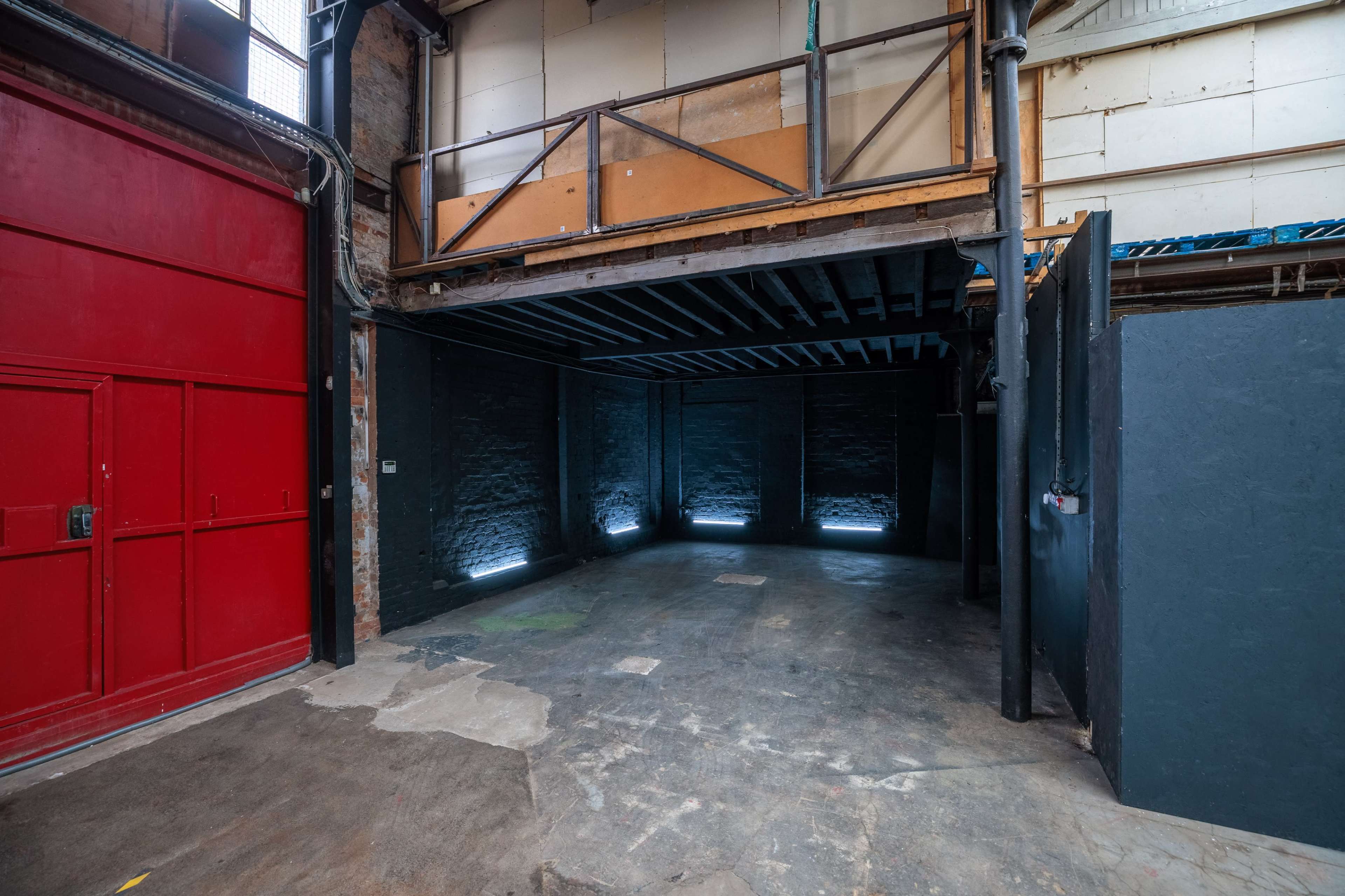 The image shows an empty industrial space with a concrete floor, exposed brick walls, and minimal lighting.