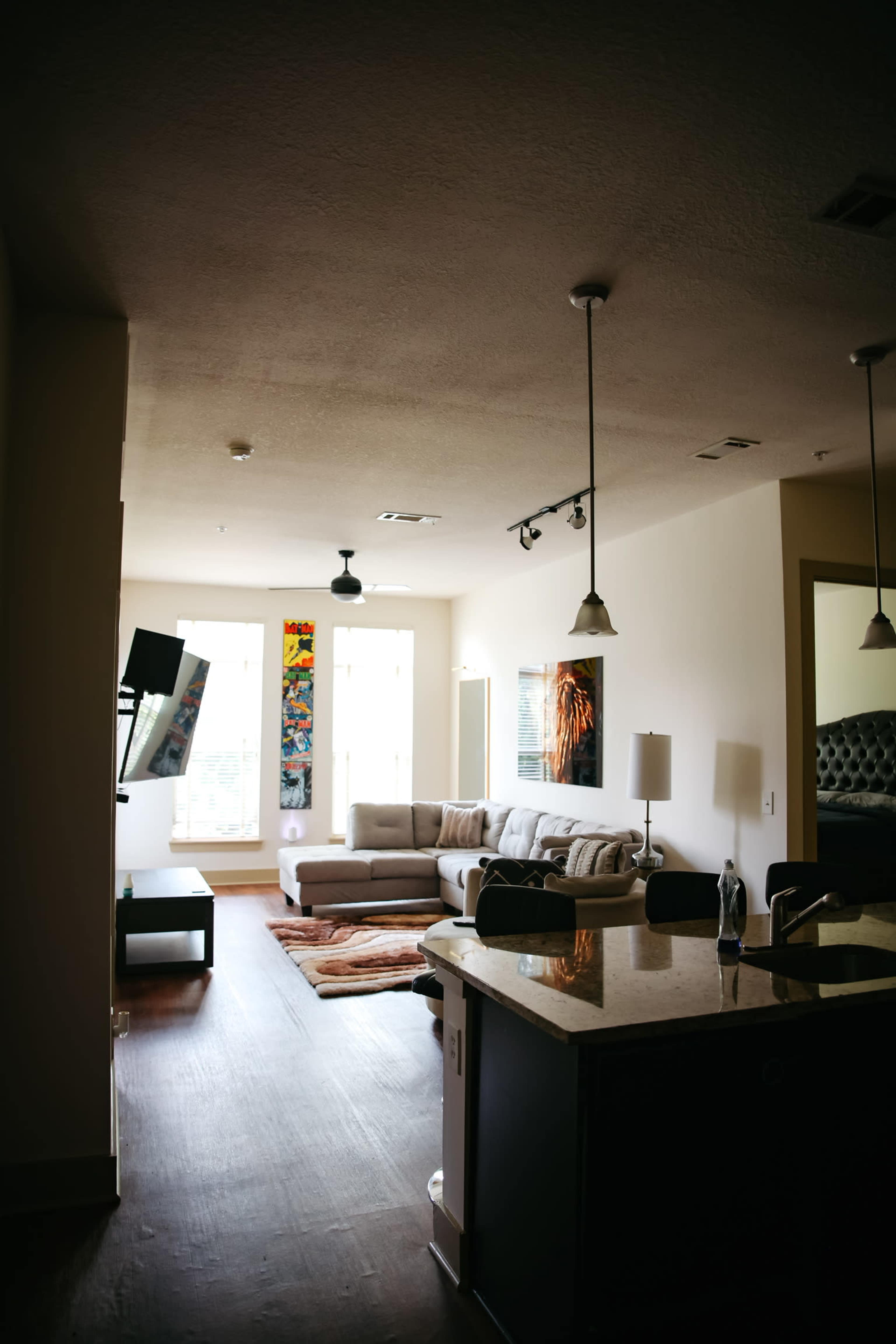 The image shows a modern living room with a sectional sofa, a coffee table, and large windows, illuminated by pendant lights.