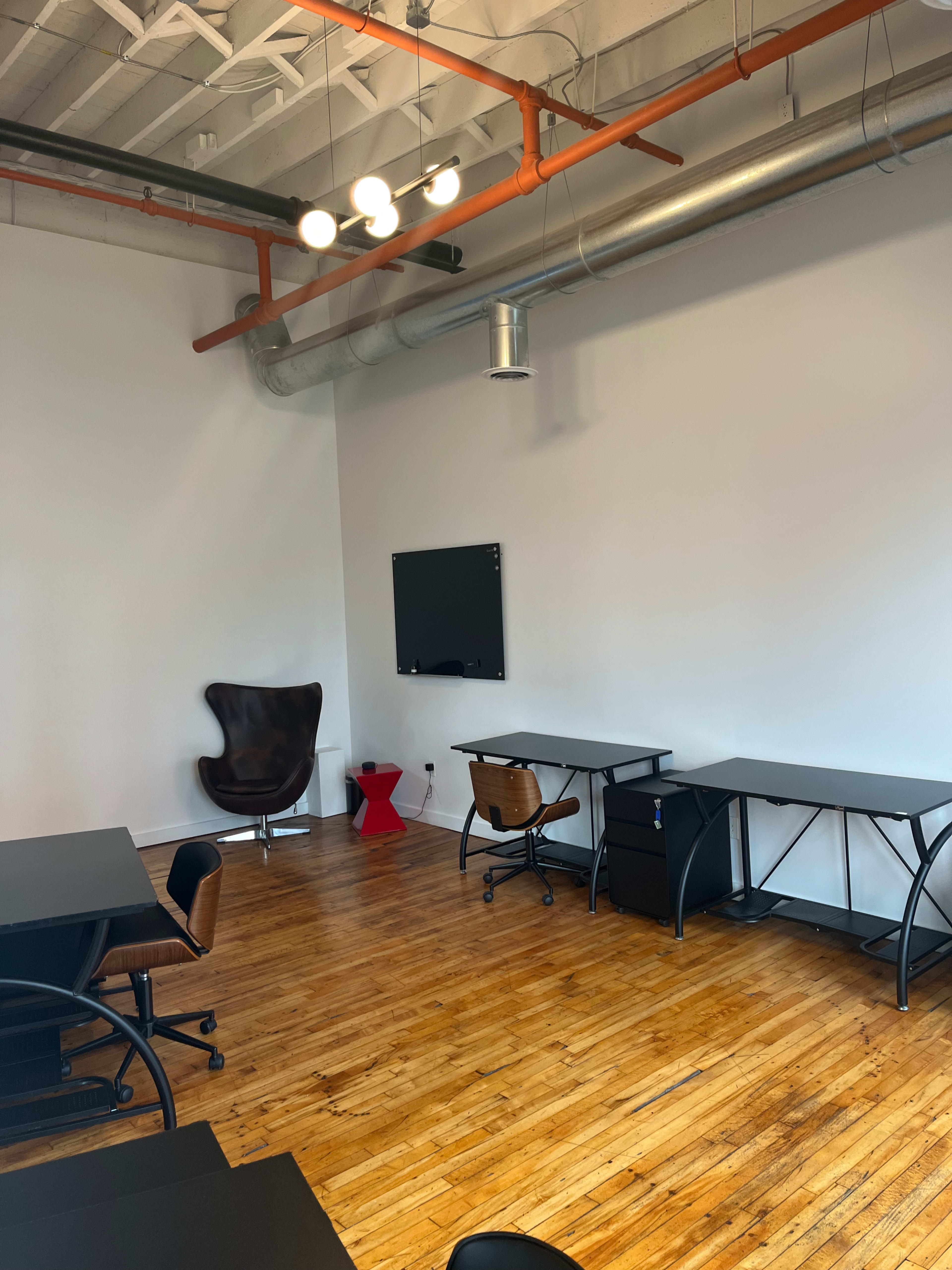 An office space with wooden floors, a large TV mounted on the wall, two desks, and a brown chair in the corner.