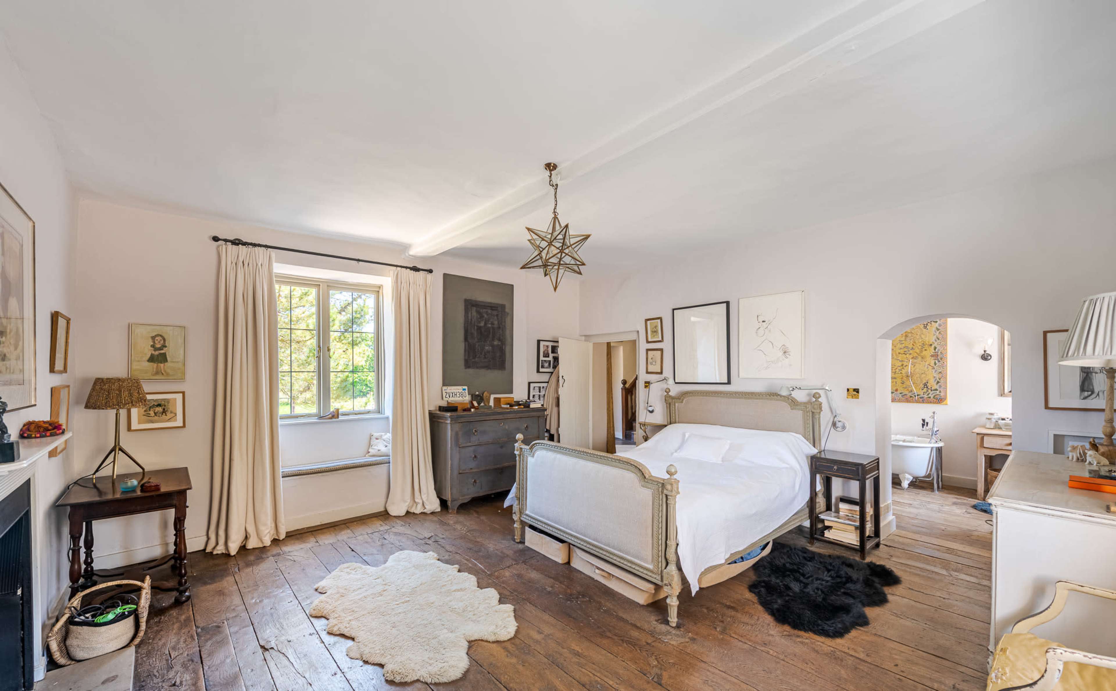 The room features a large bed, wooden flooring, and a window with natural light, accompanied by a few decorative items and a rug.