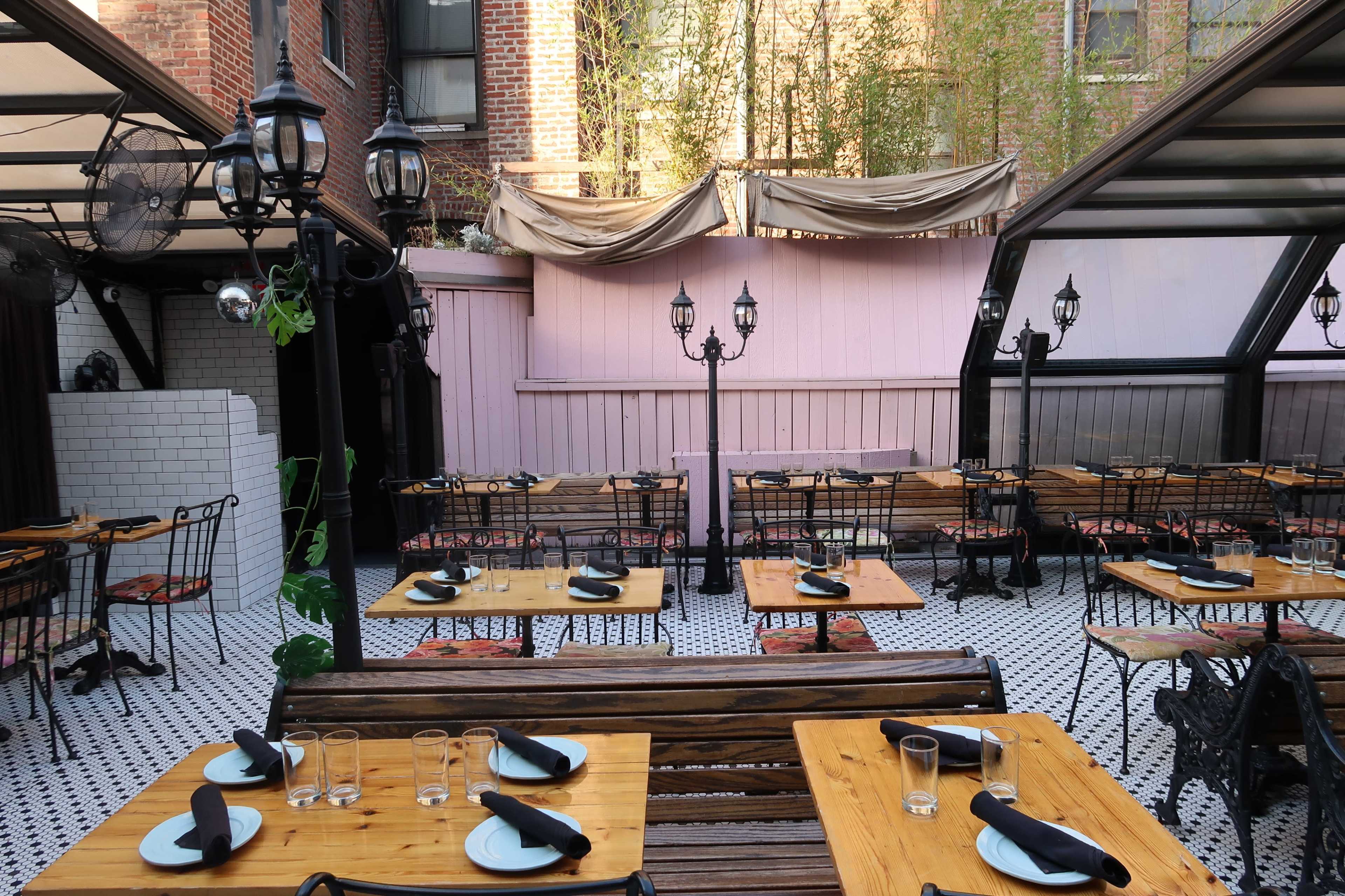An outdoor dining area with wooden tables and black chairs arranged under decorative lanterns and a canopy.