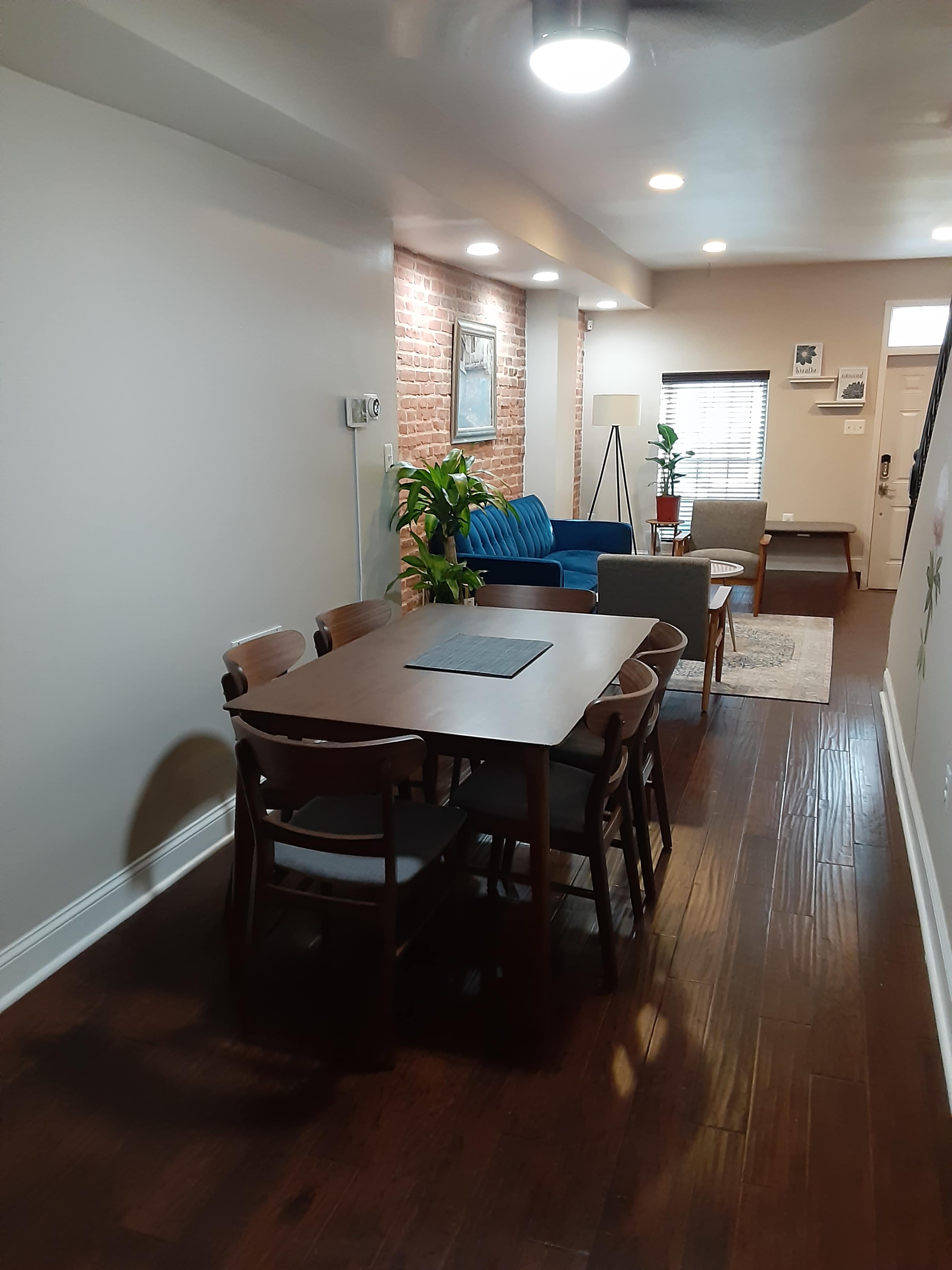 A semi-open living space with a wooden dining table and chairs, a blue couch, a green plant, and light-colored walls.