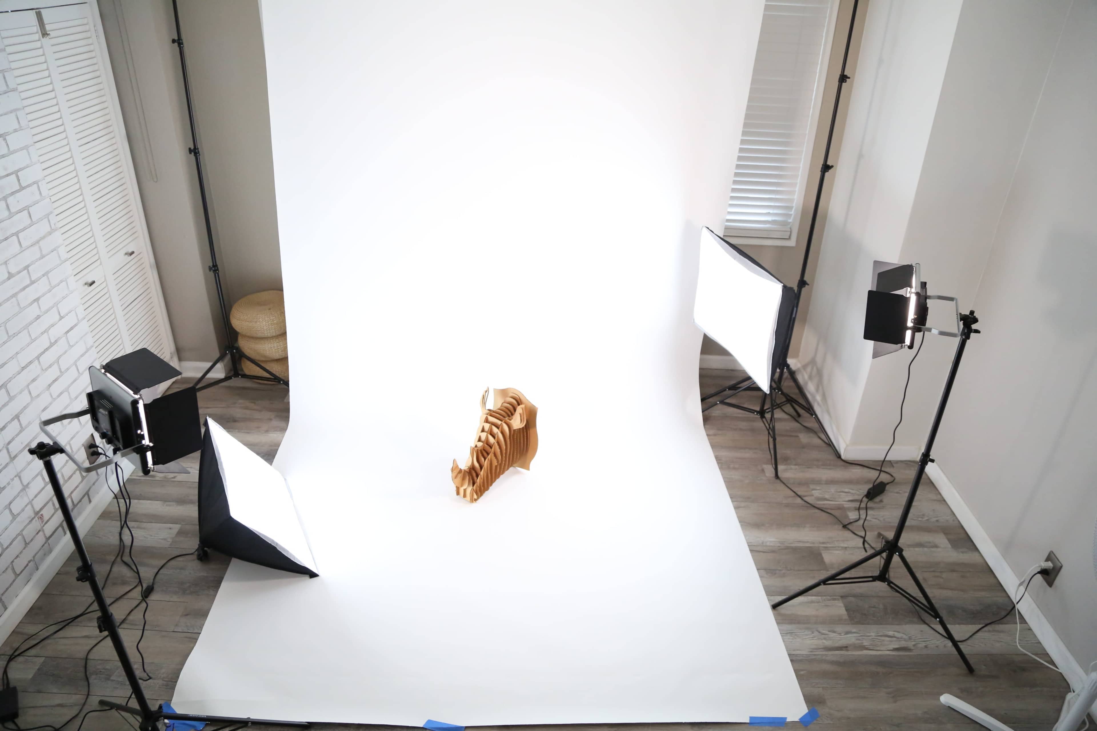 The image shows a photography setup with bright lights and a blank backdrop, featuring a wooden object positioned at the center.