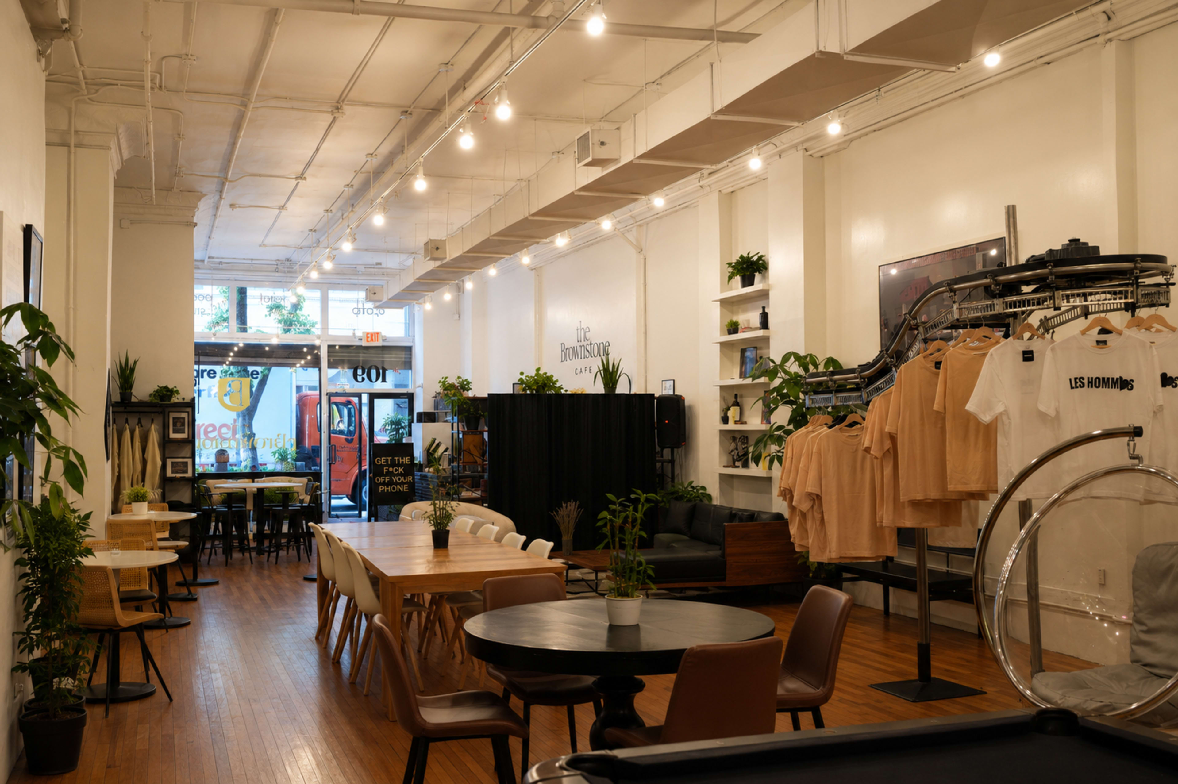 The image shows a brightly lit indoor space featuring a clothing store with racks of apparel, seating areas, and various plants throughout.