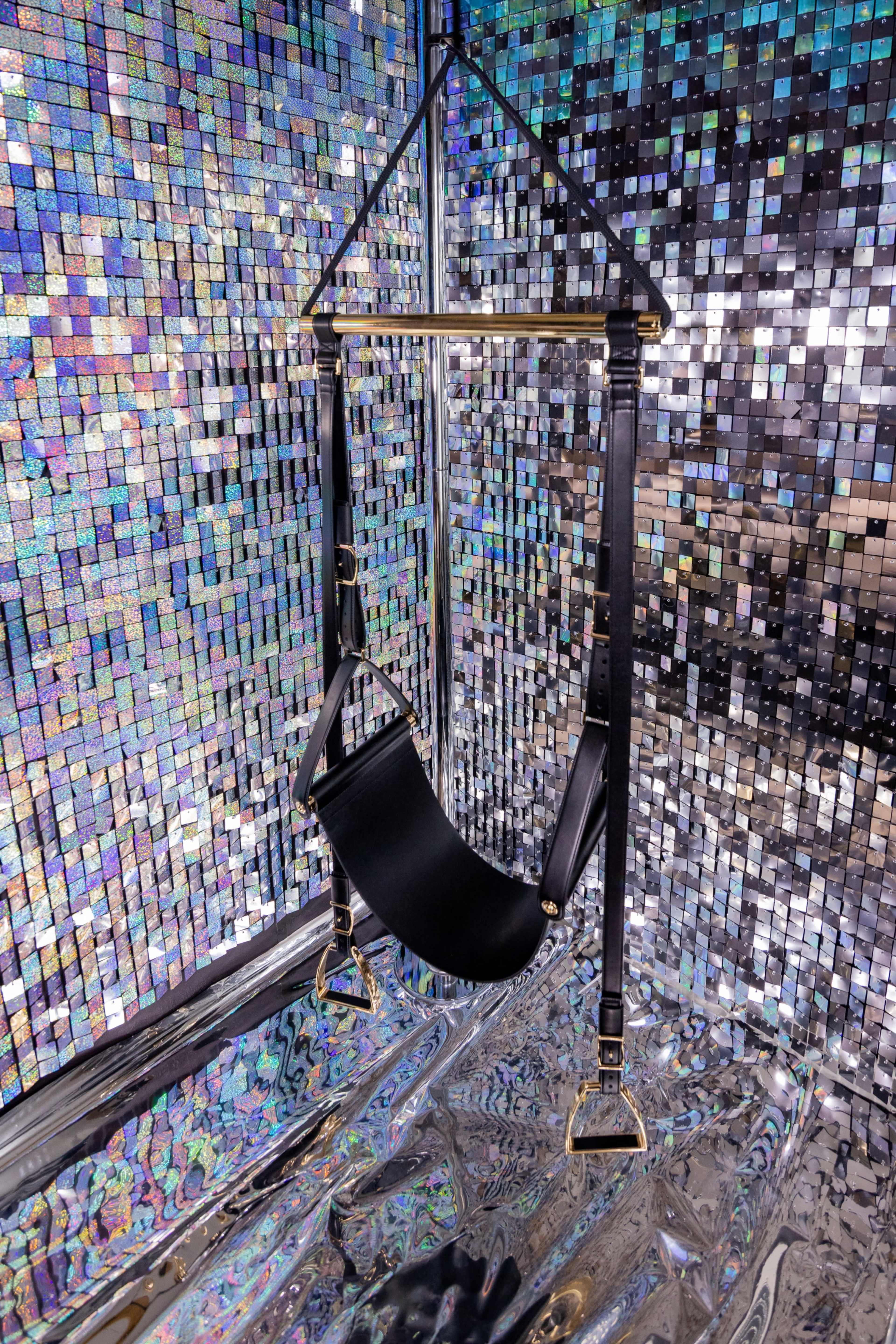 A black suspension hammock is mounted against a reflective, multicolored tiled wall.