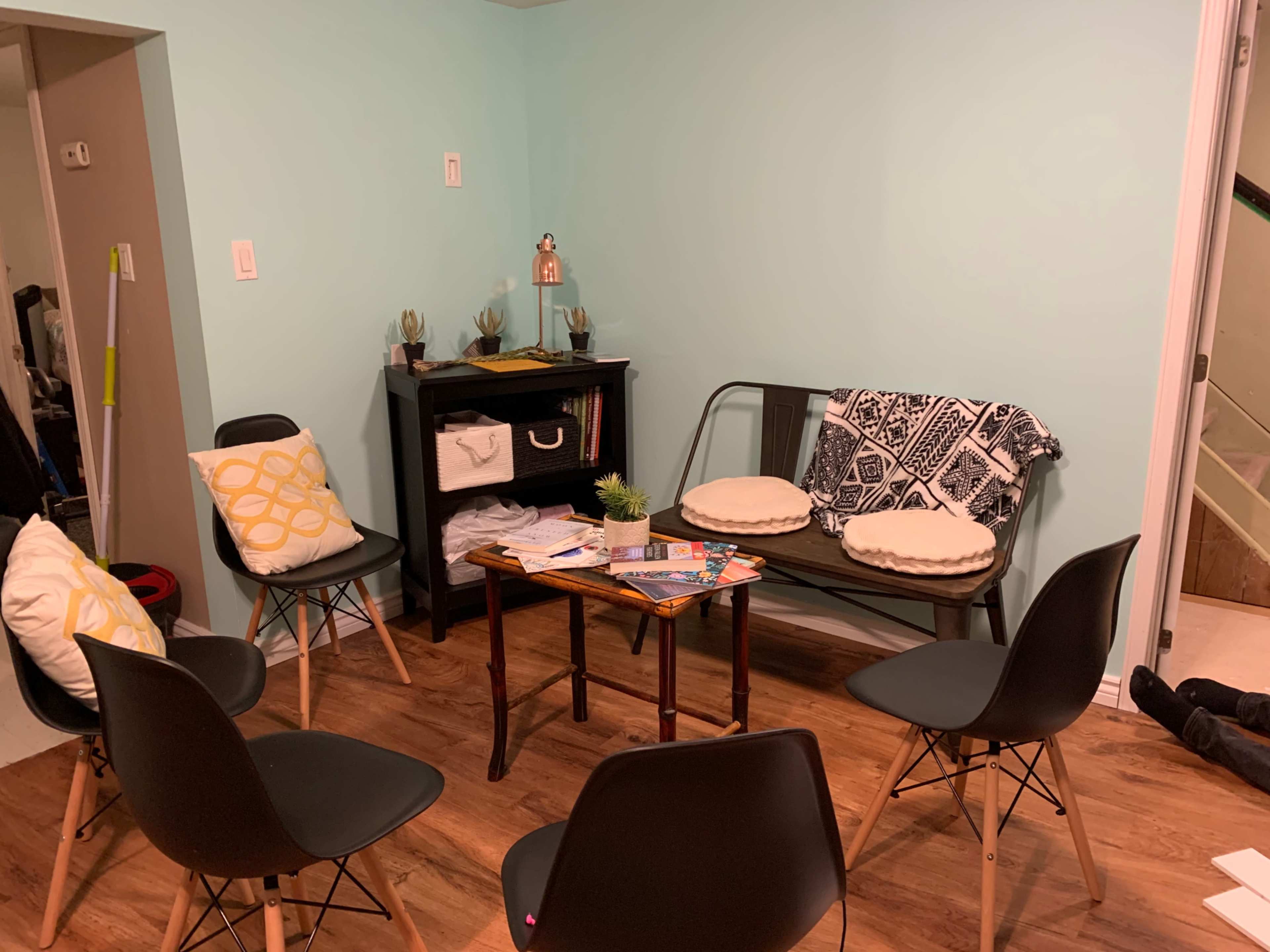 A small seating area features a table surrounded by five chairs, a couch, and a black storage unit against a light blue wall.