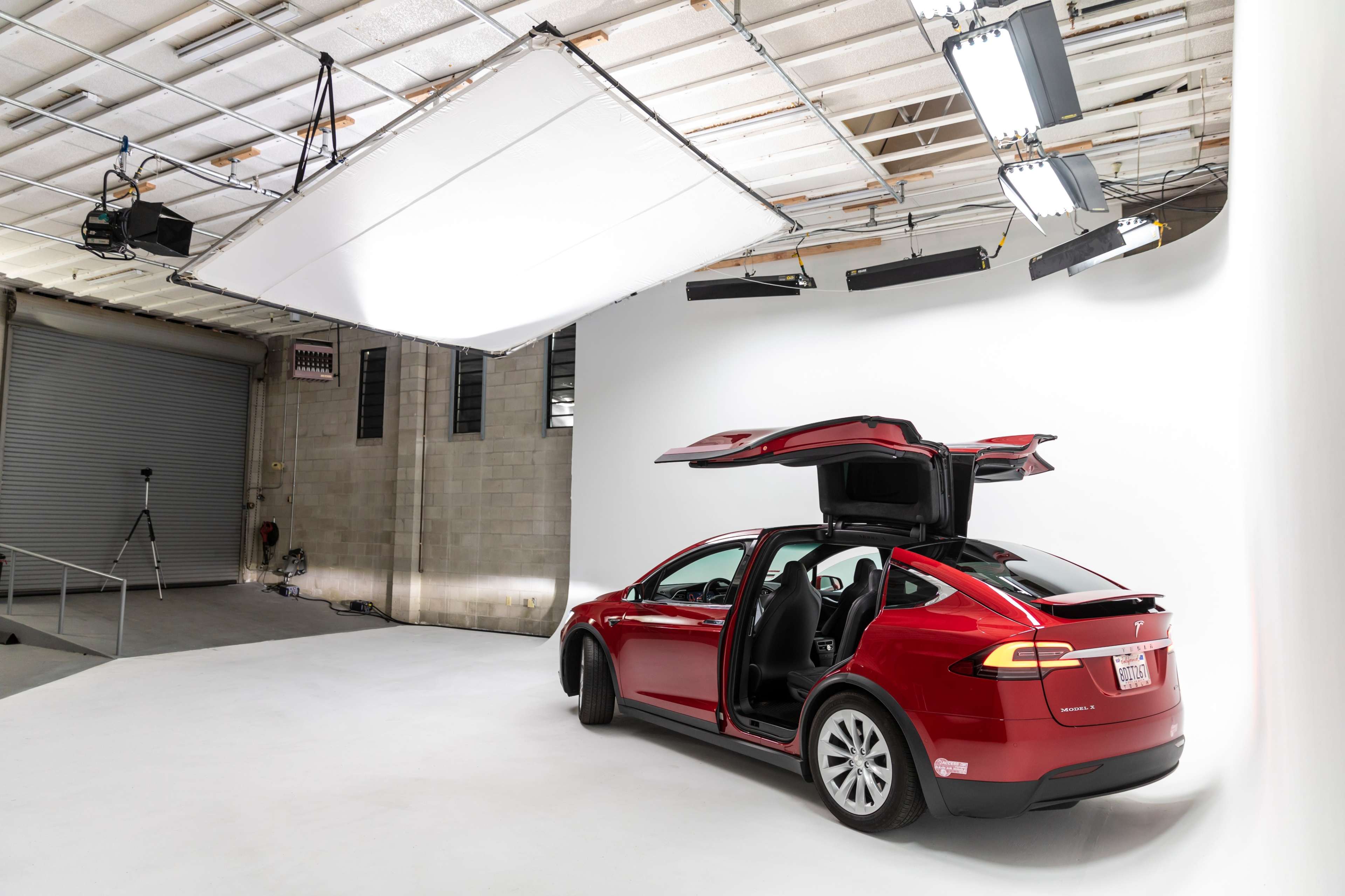 A red Tesla Model X with its rear doors opened is positioned in a well-lit photography studio with a white backdrop.