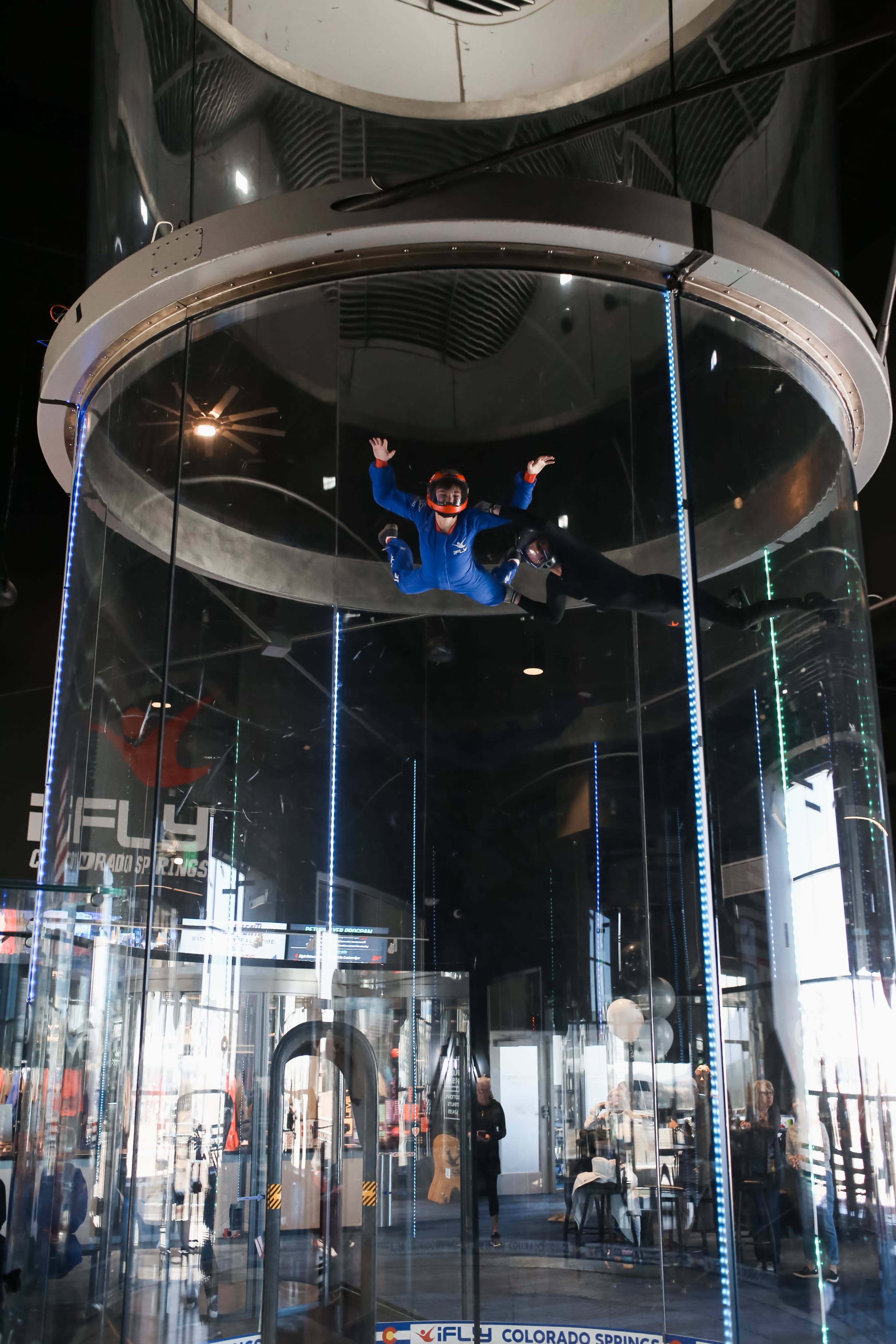 A person wearing a blue jumpsuit and helmet is practicing indoor skydiving inside a vertical wind tunnel.