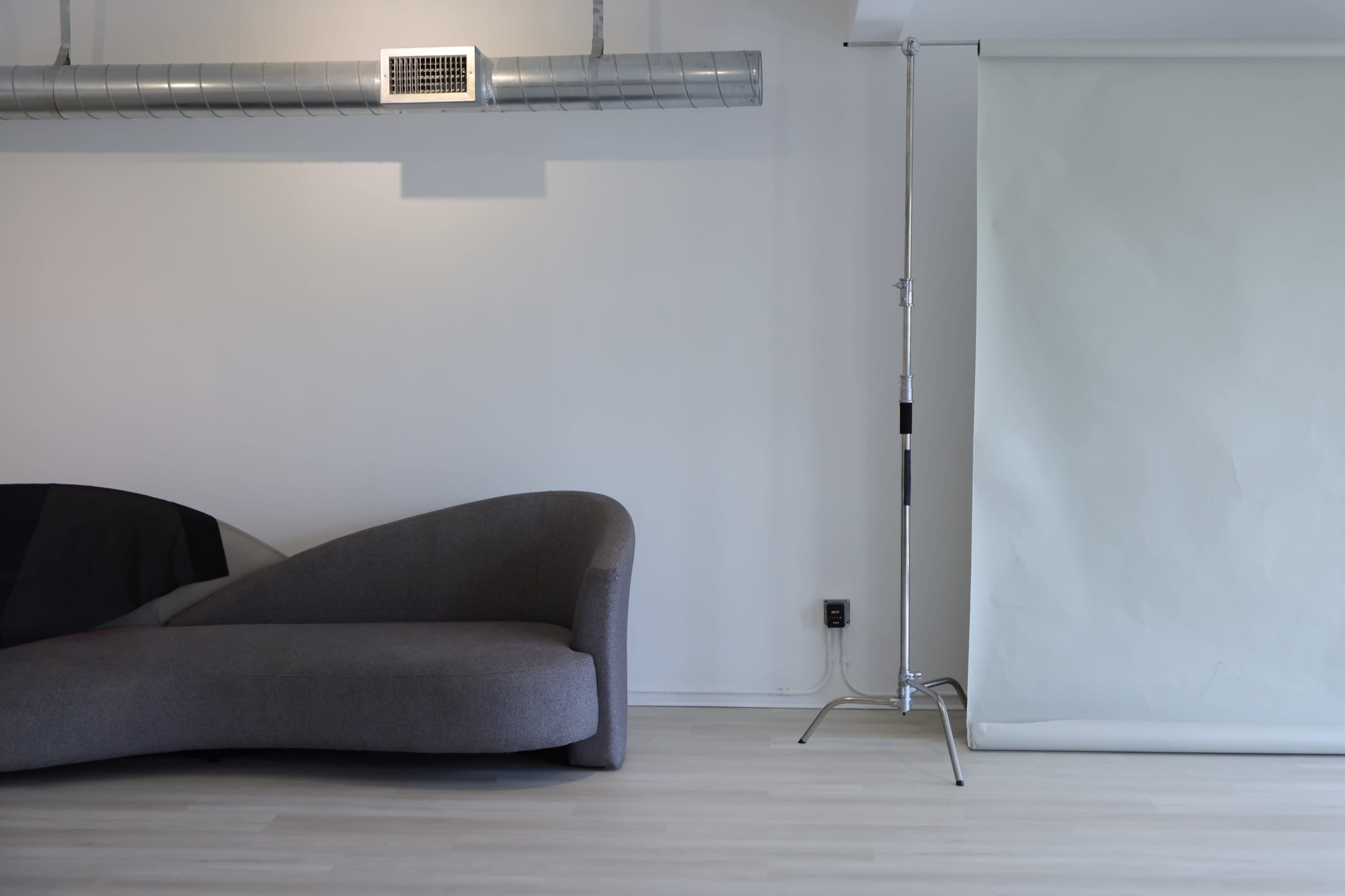 The image shows a modern, minimalist room featuring a curved gray sofa on one side and a backdrop stand with a light-colored backdrop on the other.