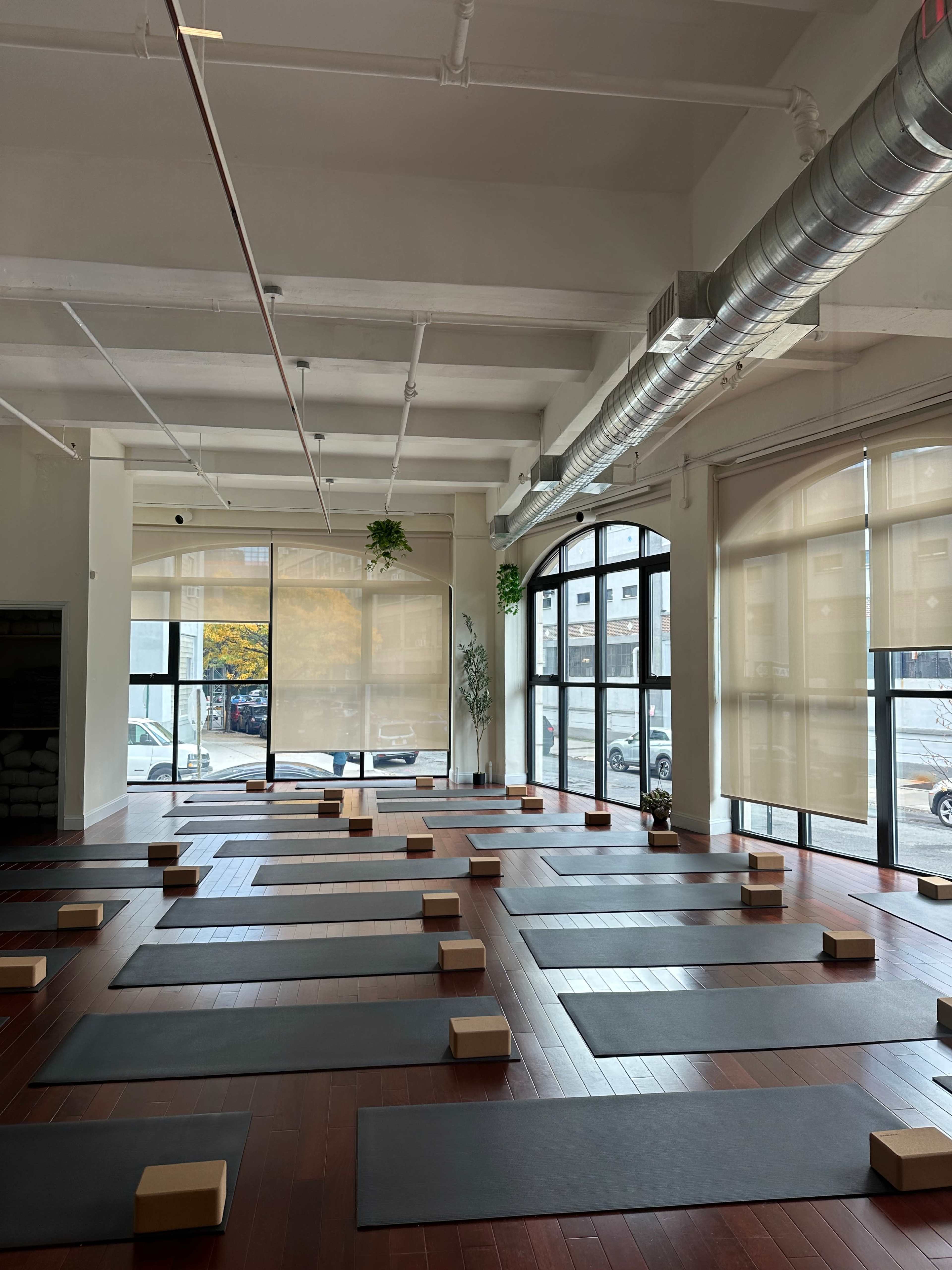 A spacious yoga studio with neatly arranged mats, blocks, and large windows letting in natural light.
