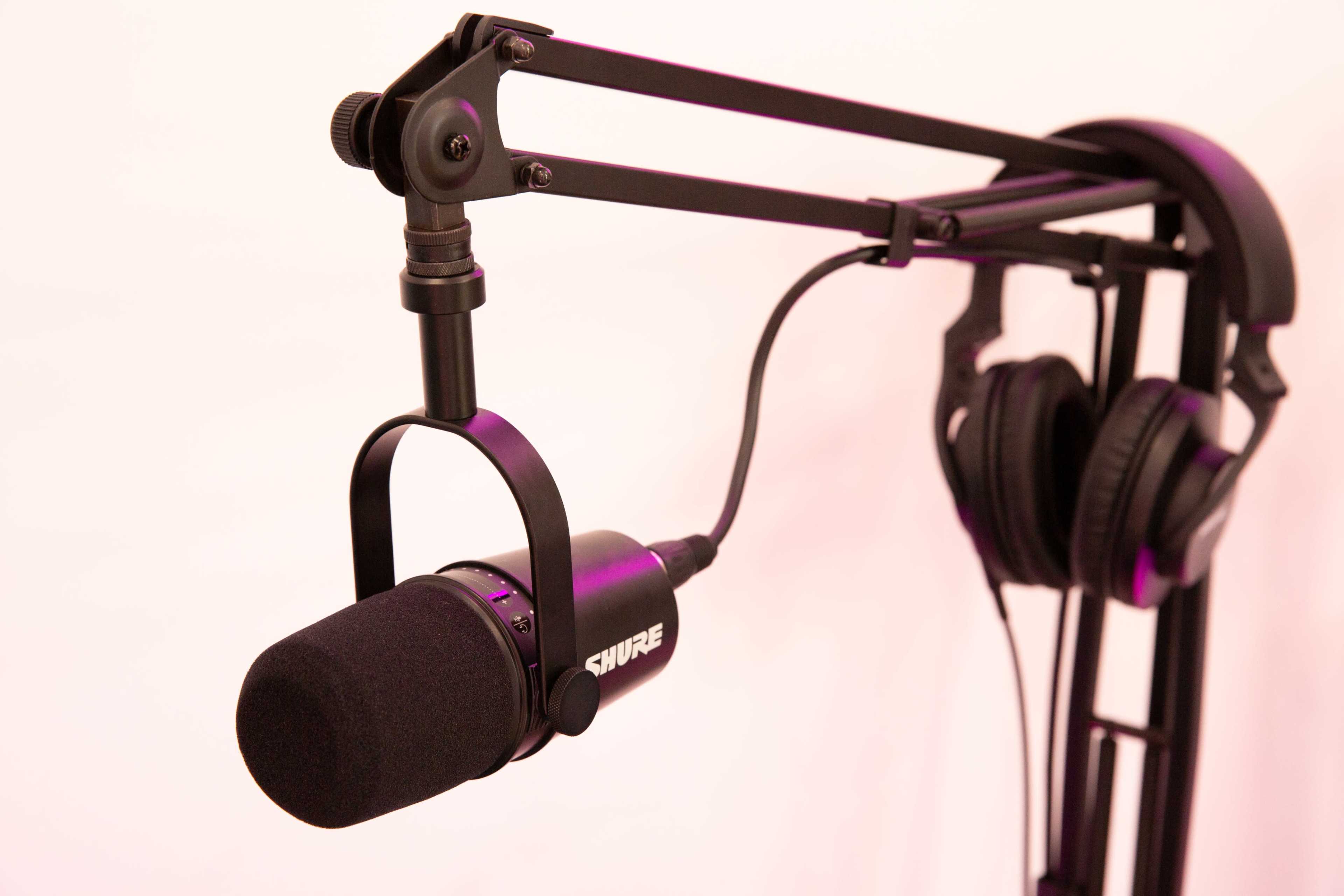 A black Shure microphone is mounted on an adjustable boom arm next to a pair of over-ear headphones.