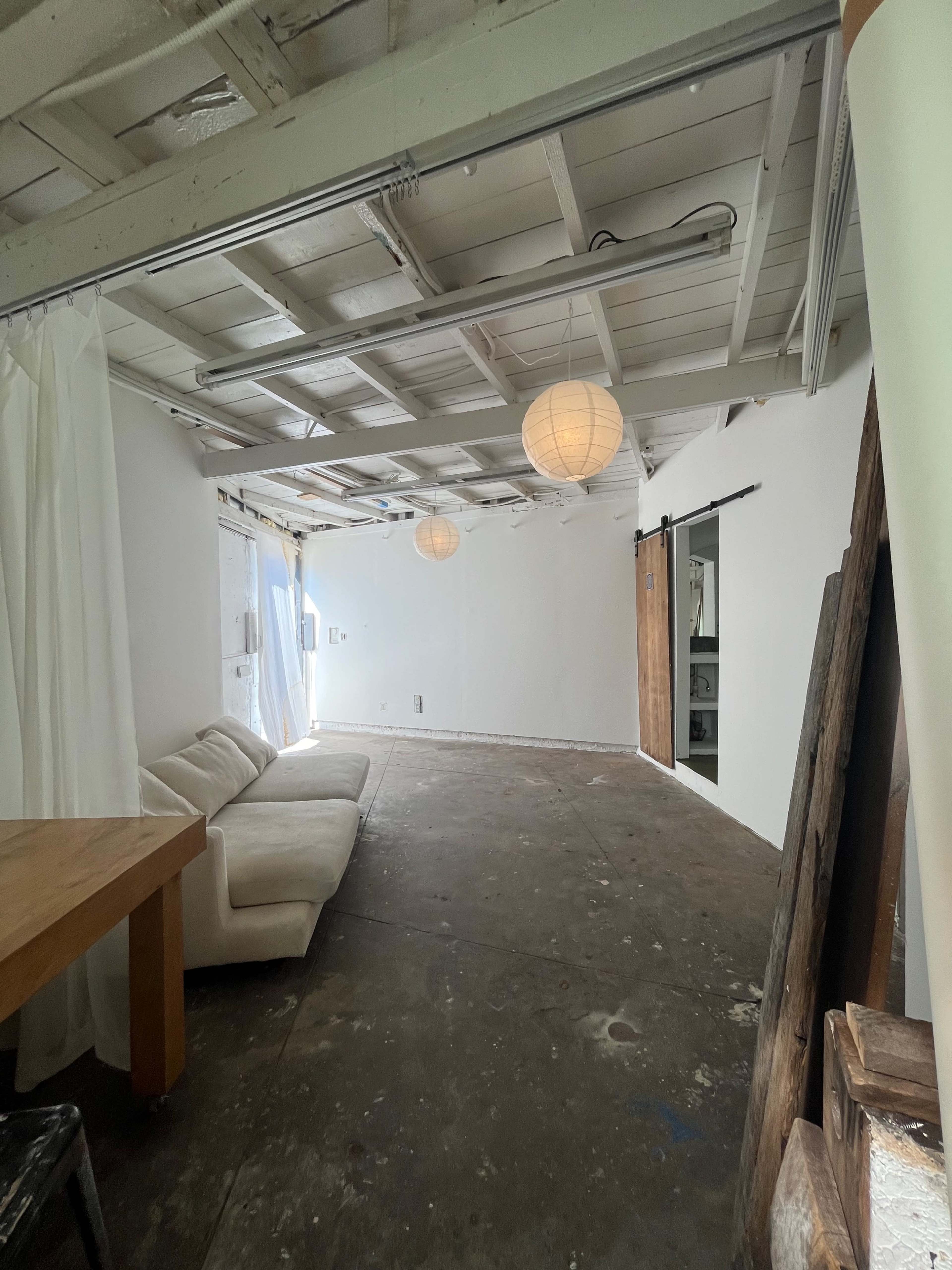 A spacious, minimalist room with a white interior, a light-colored sofa, and paper lanterns hanging from the ceiling.