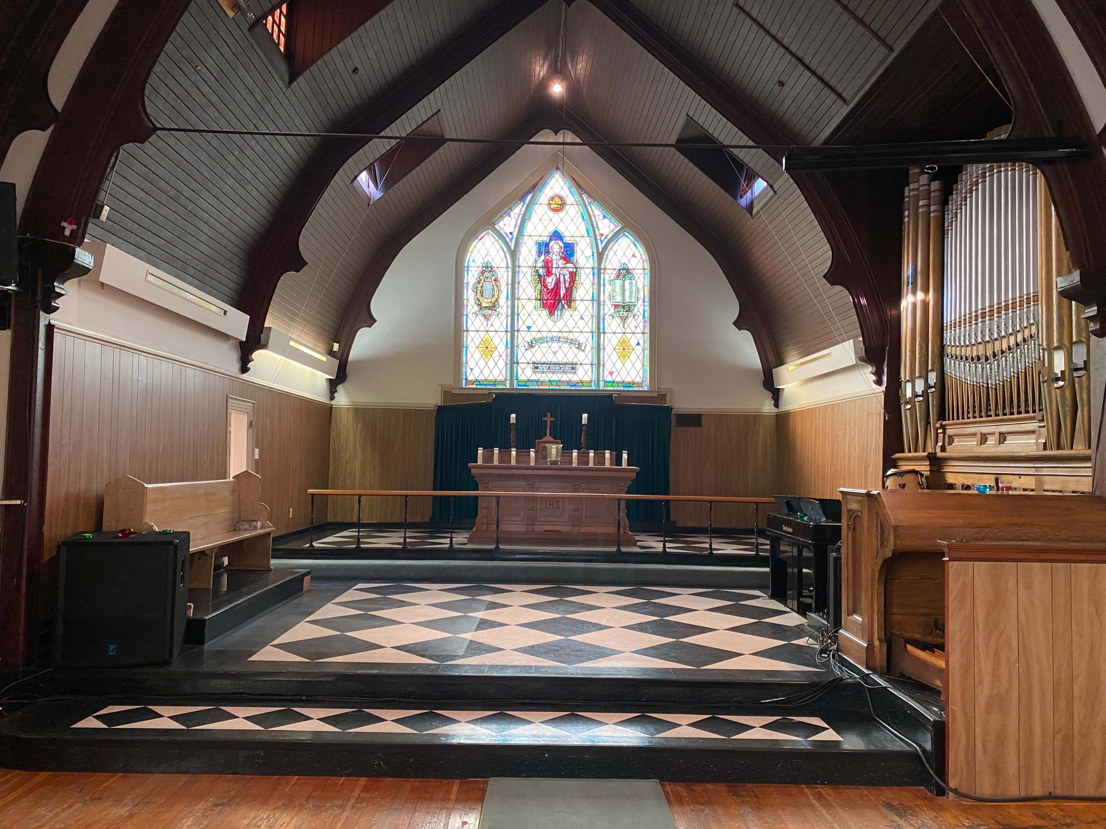 The interior of a church features a wooden altar, a colorful stained glass window, and an organ on the right side.