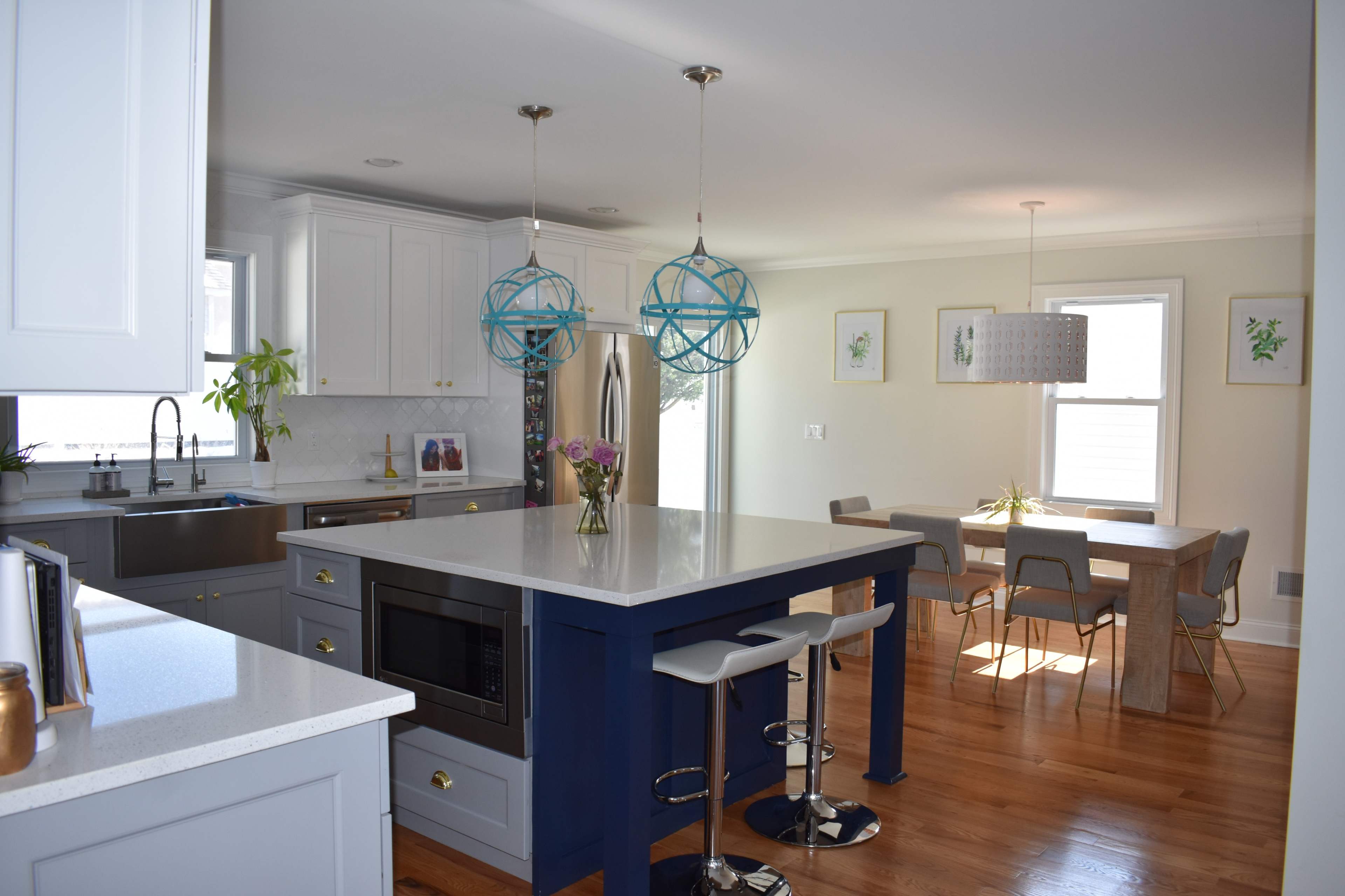 A modern kitchen with white cabinetry, a blue kitchen island, pendant lights, and a dining area featuring a wooden table and gray chairs.
