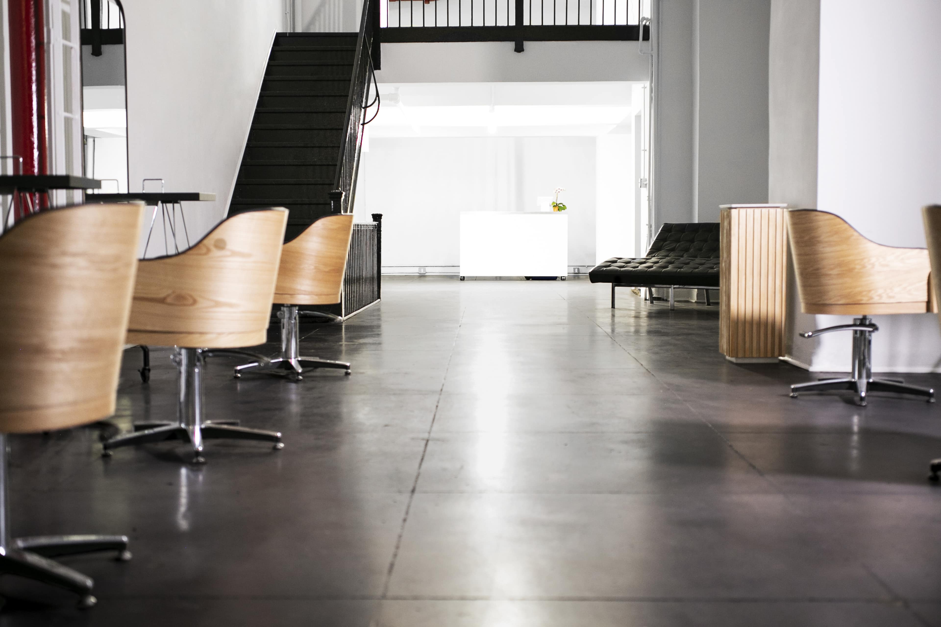 A modern indoor space with wooden chairs and a staircase leading to an upper level.