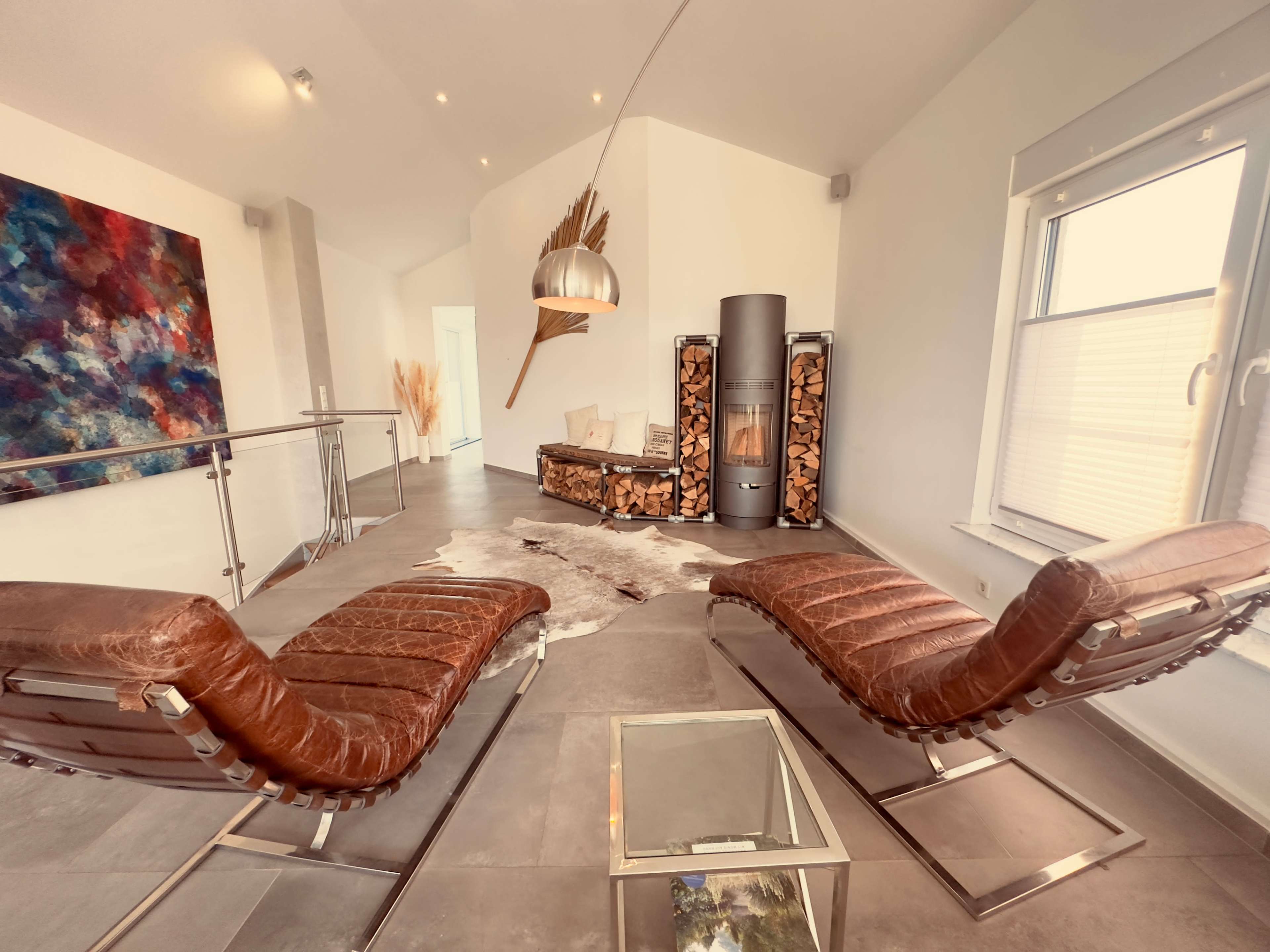 The image shows a modern indoor space with two brown lounge chairs facing a stylish fireplace, a decorative wall art, and a glass coffee table.