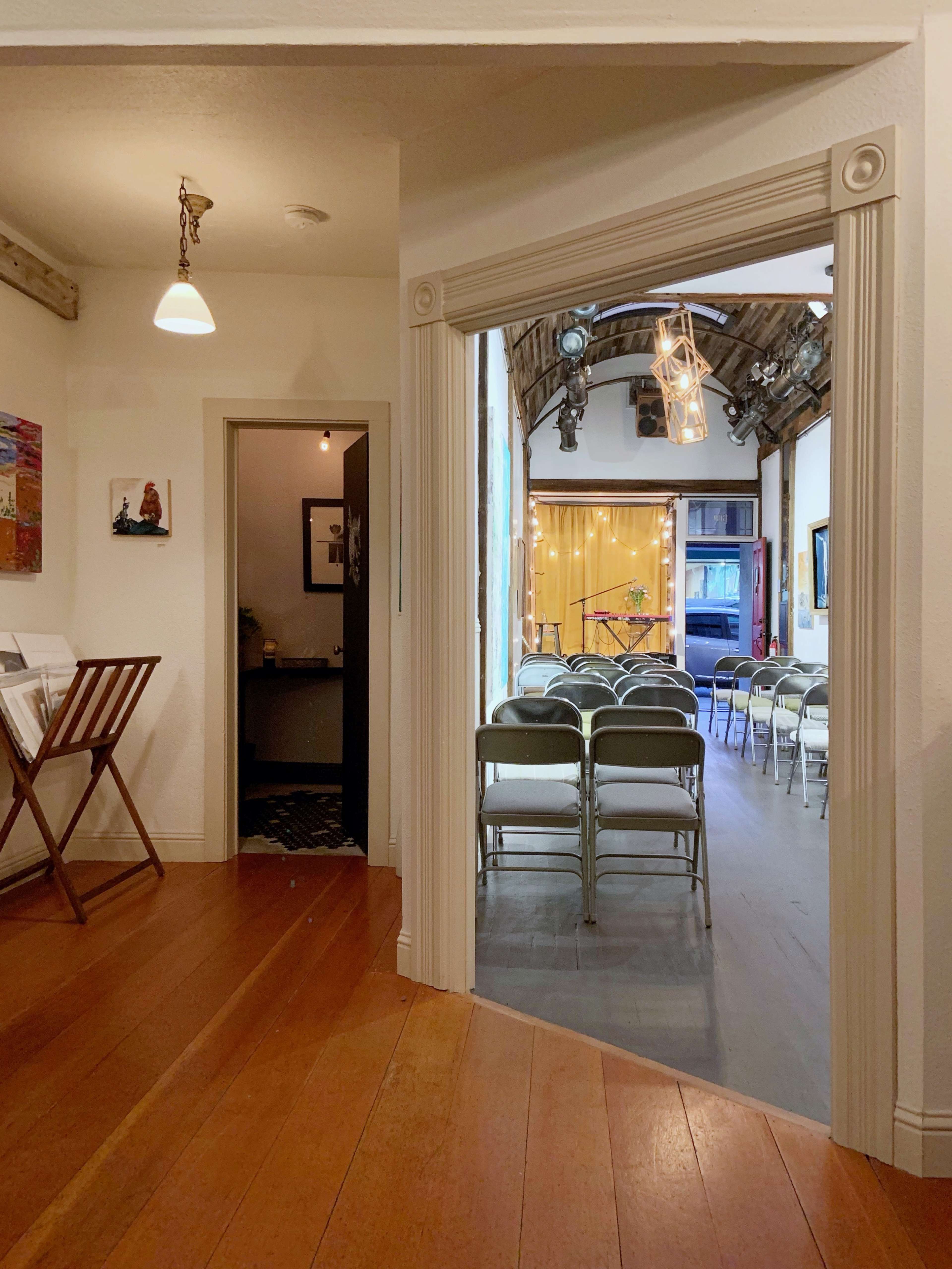 A corridor leading to a room with chairs arranged for an event, framed by white walls and wooden accents.