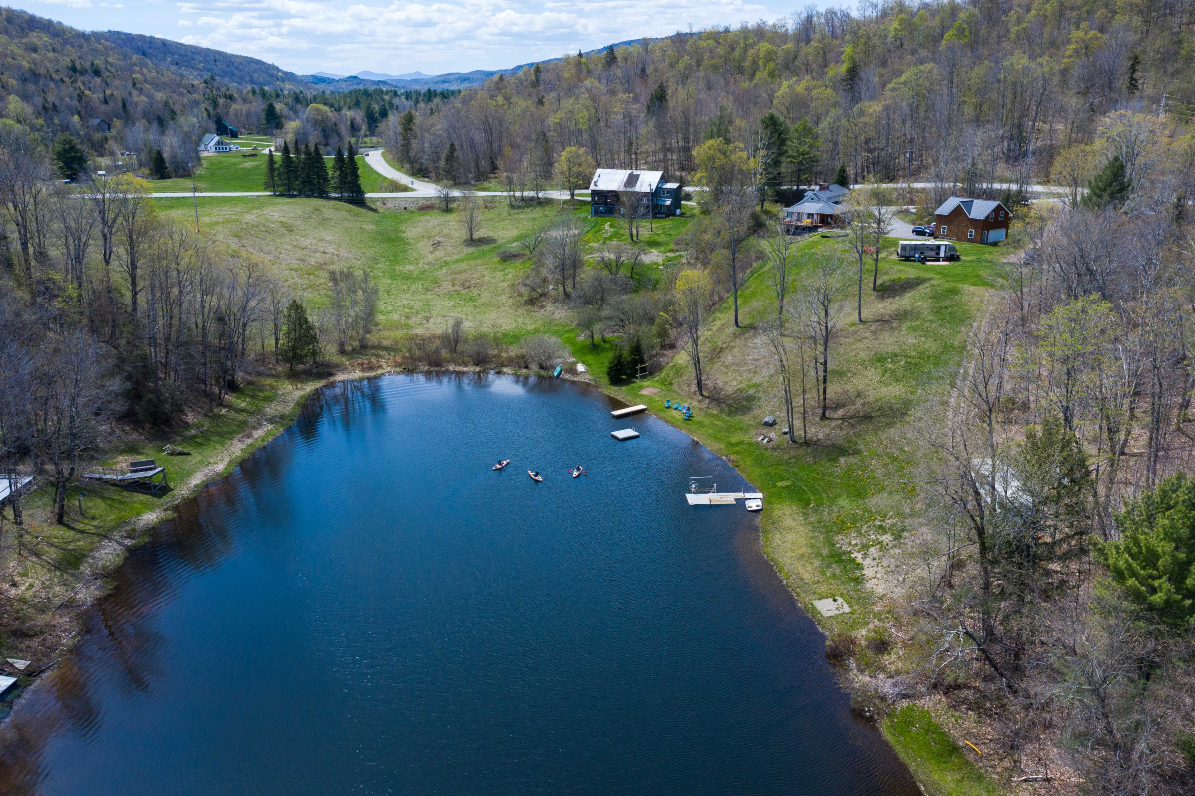 A serene pond surrounded by trees and houses, with several people kayaking on the water.