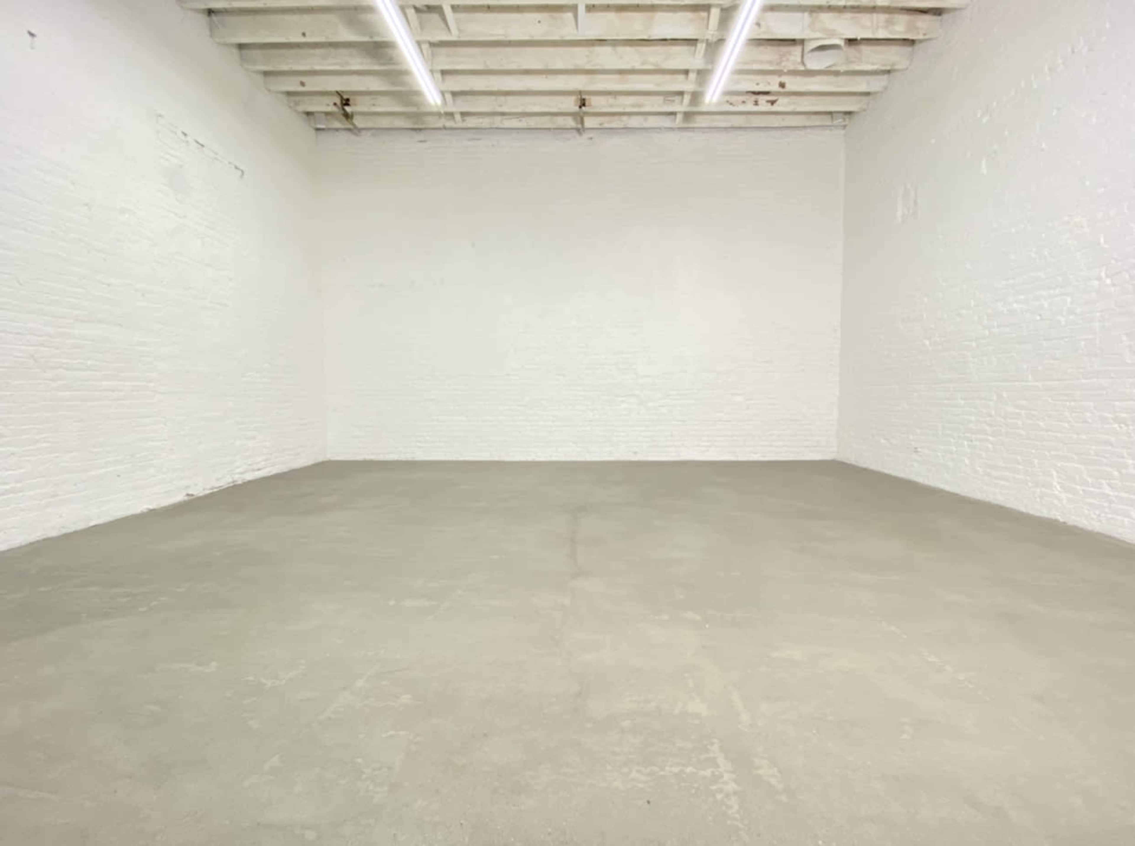 A large, empty room with white brick walls and a concrete floor, illuminated by overhead lights.