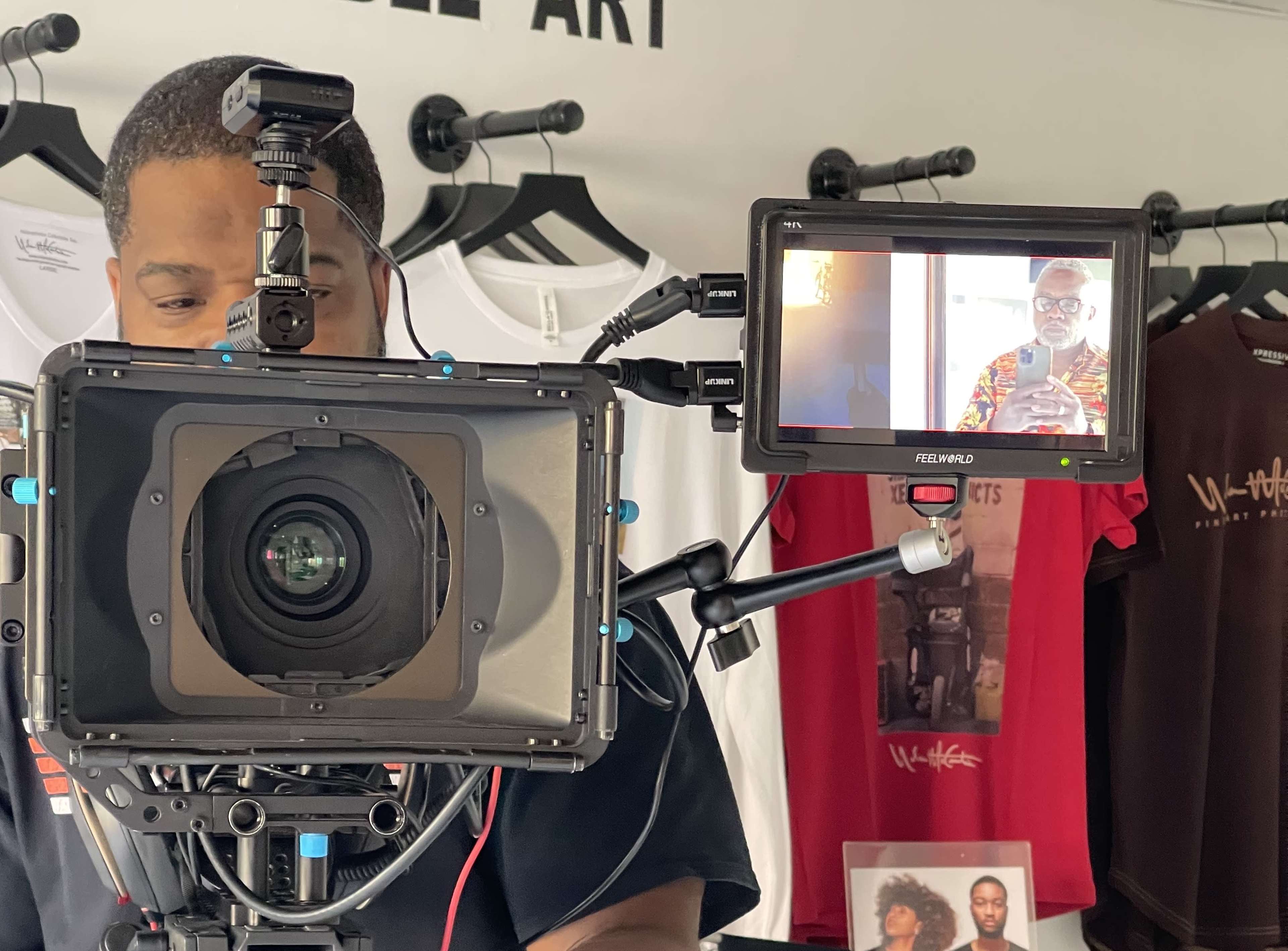 A camera is set up in front of a clothing display featuring T-shirts, while a person is being filmed on a monitor.