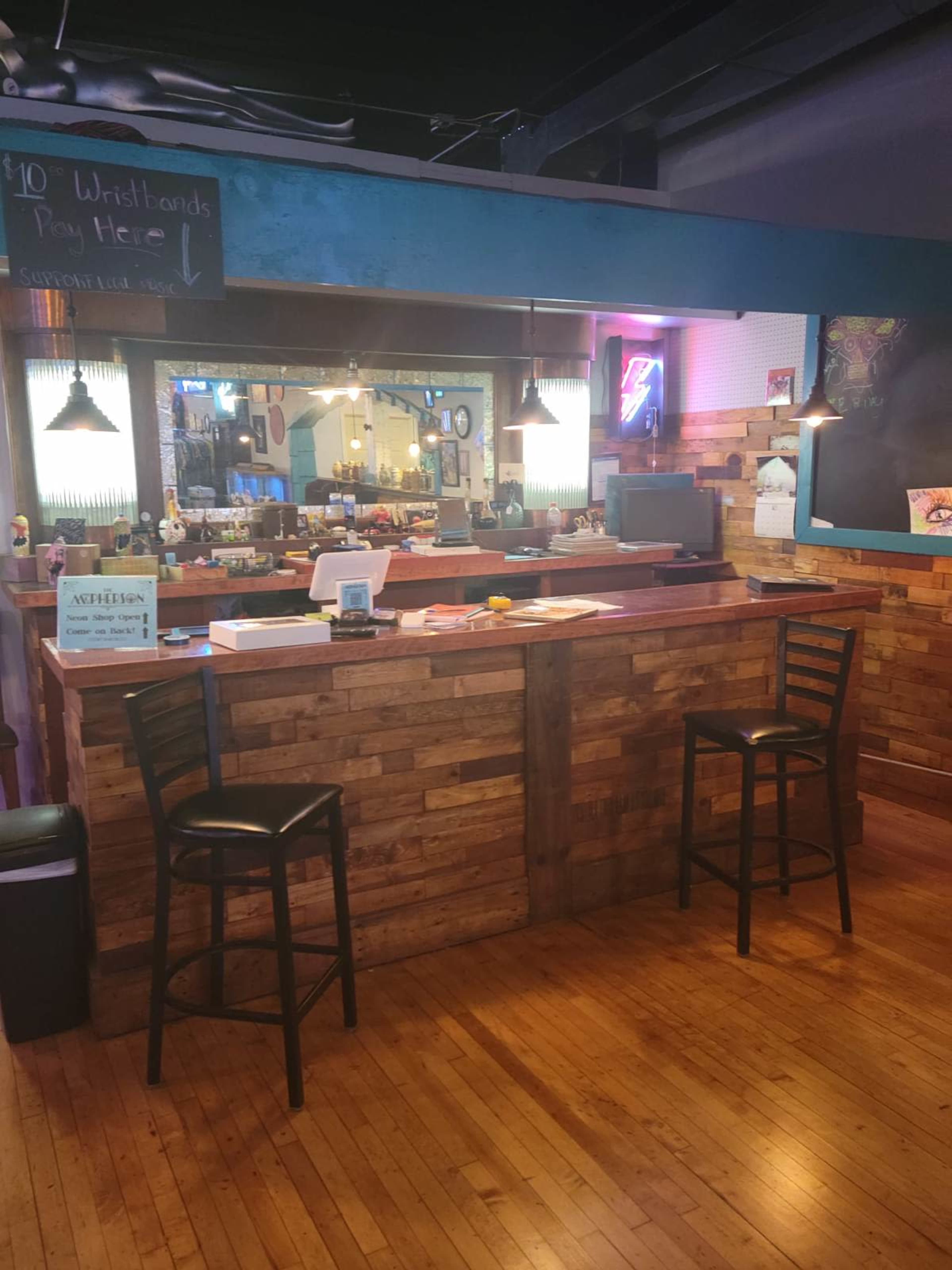 The image shows a wooden bar counter with two empty stools, set in a dimly lit establishment featuring a rustic decor style.