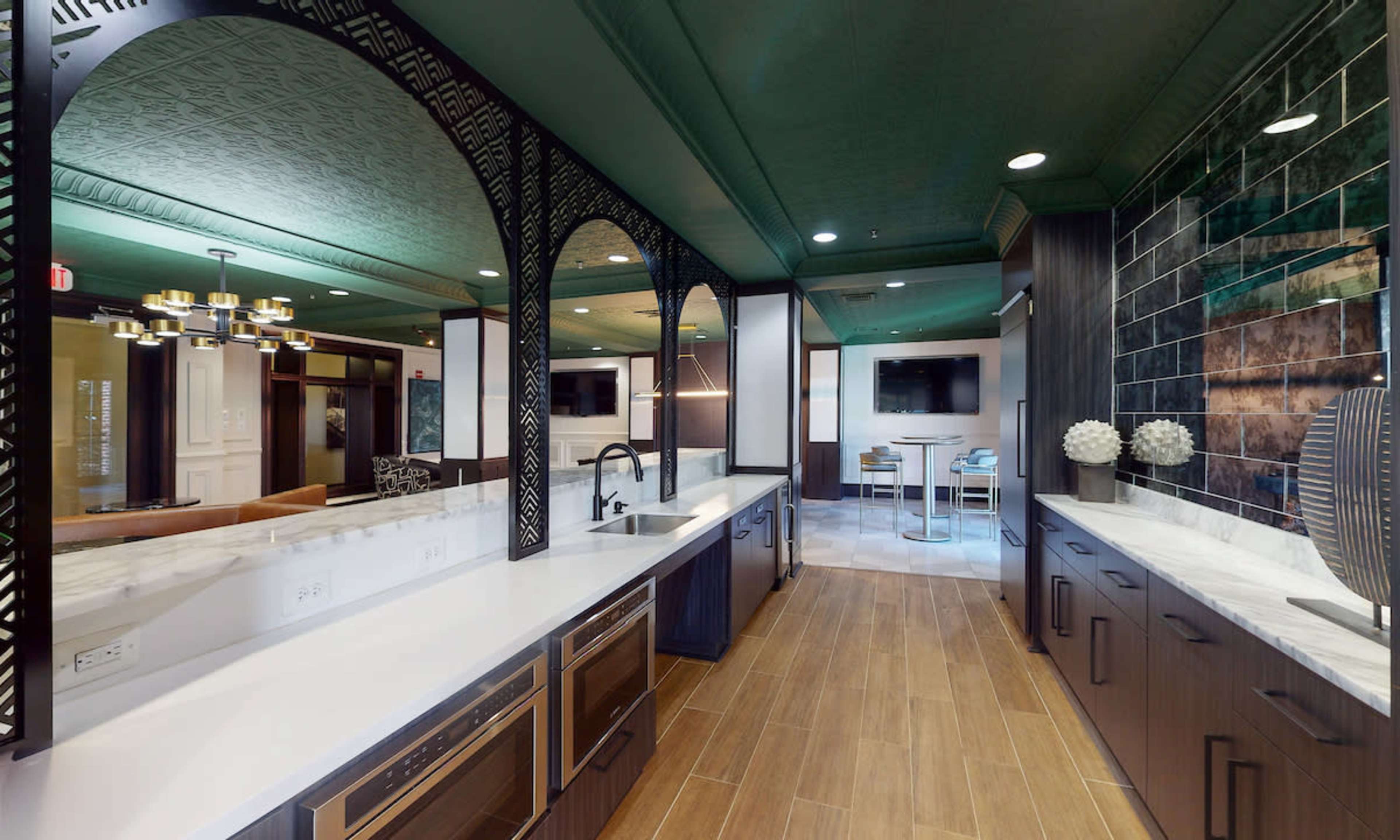 A modern kitchen with dark cabinetry, a white countertop, and an open layout that includes arches and decorative wall tiles.