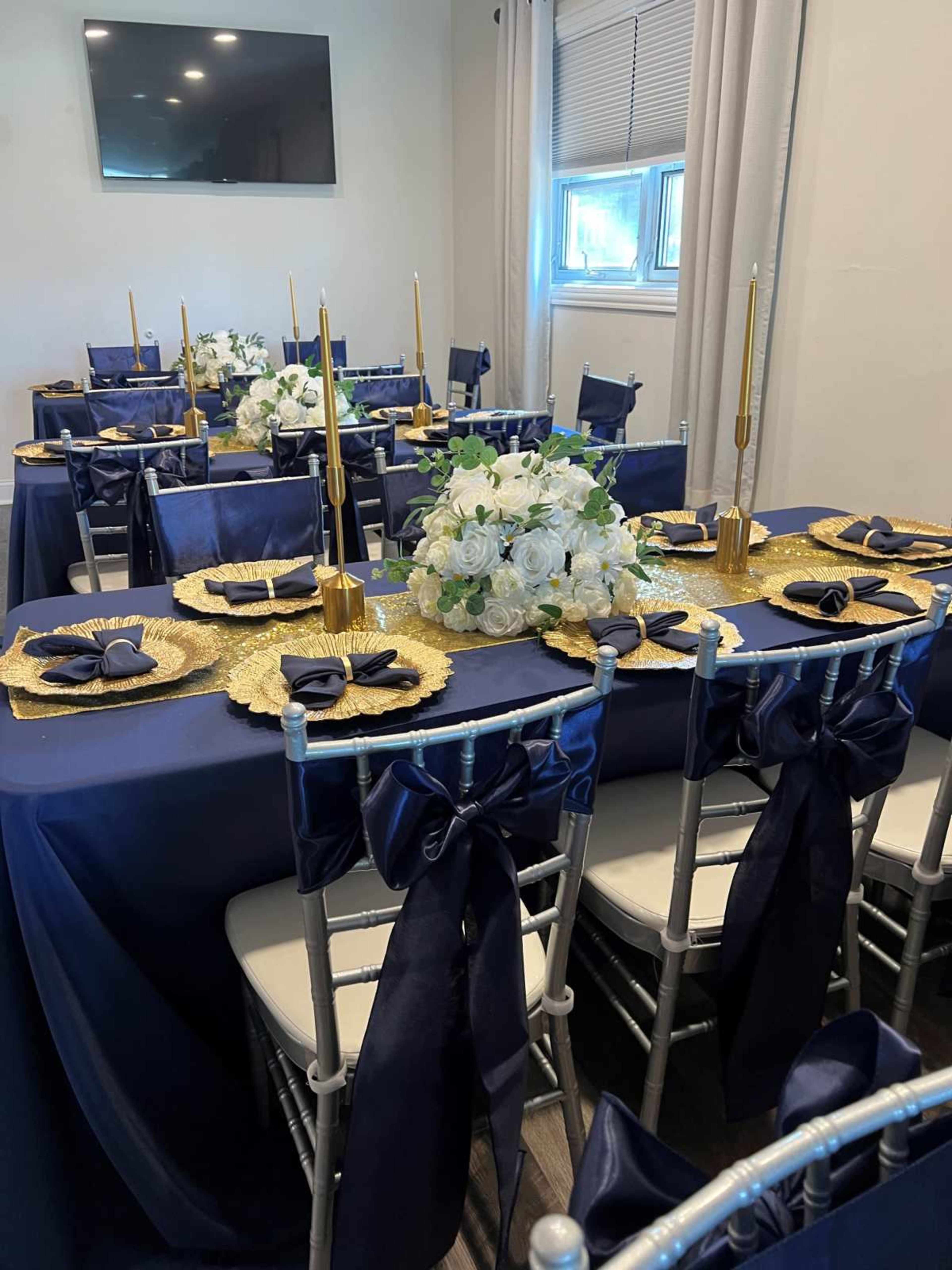 The image shows a banquet setting with navy blue and gold decorations, including a table with elegant place settings, white floral arrangements, and gold candlesticks.